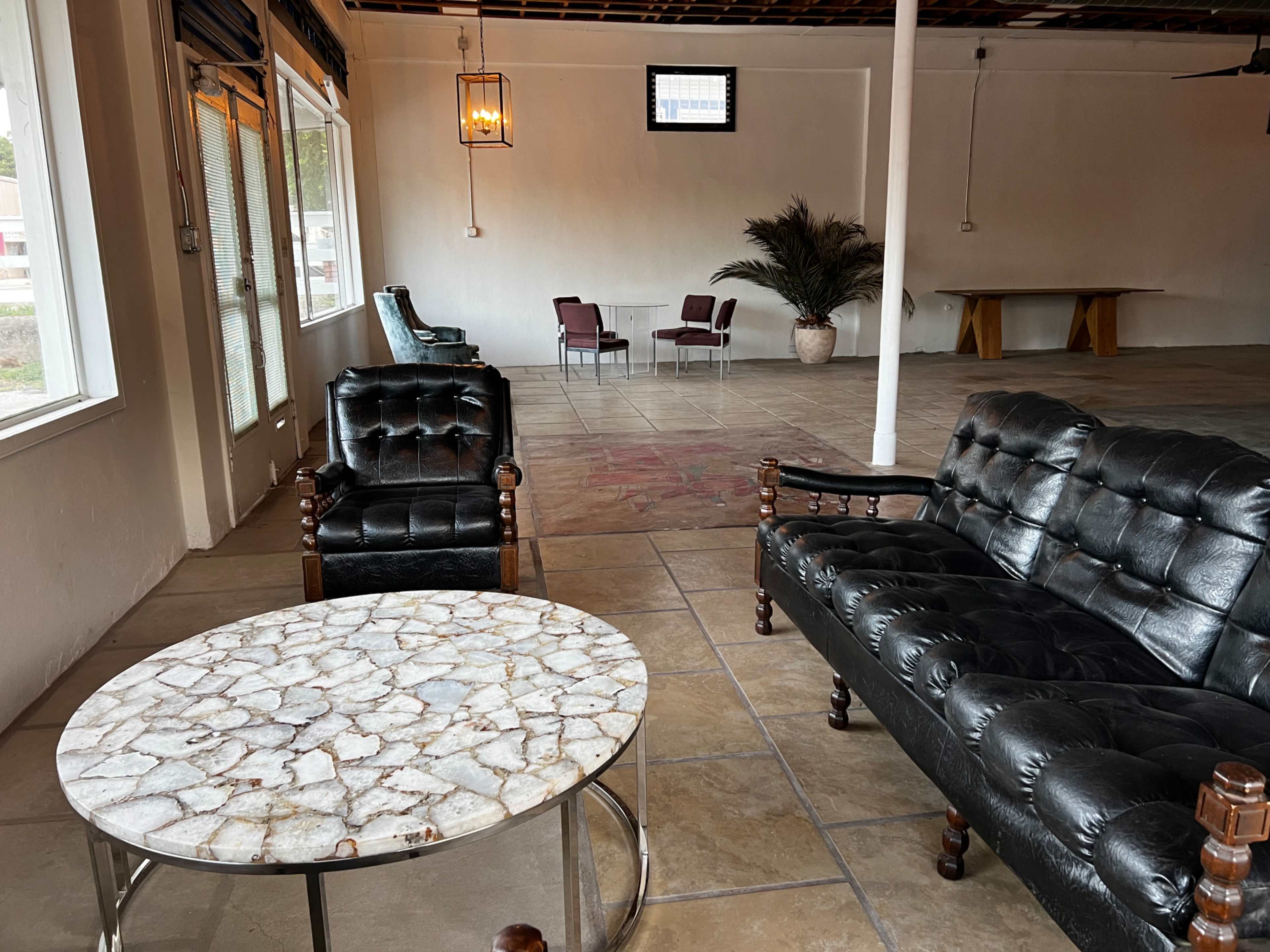 A spacious indoor seating area with two black leather couches, a round marble table, and a few chairs arranged in a minimalist design.