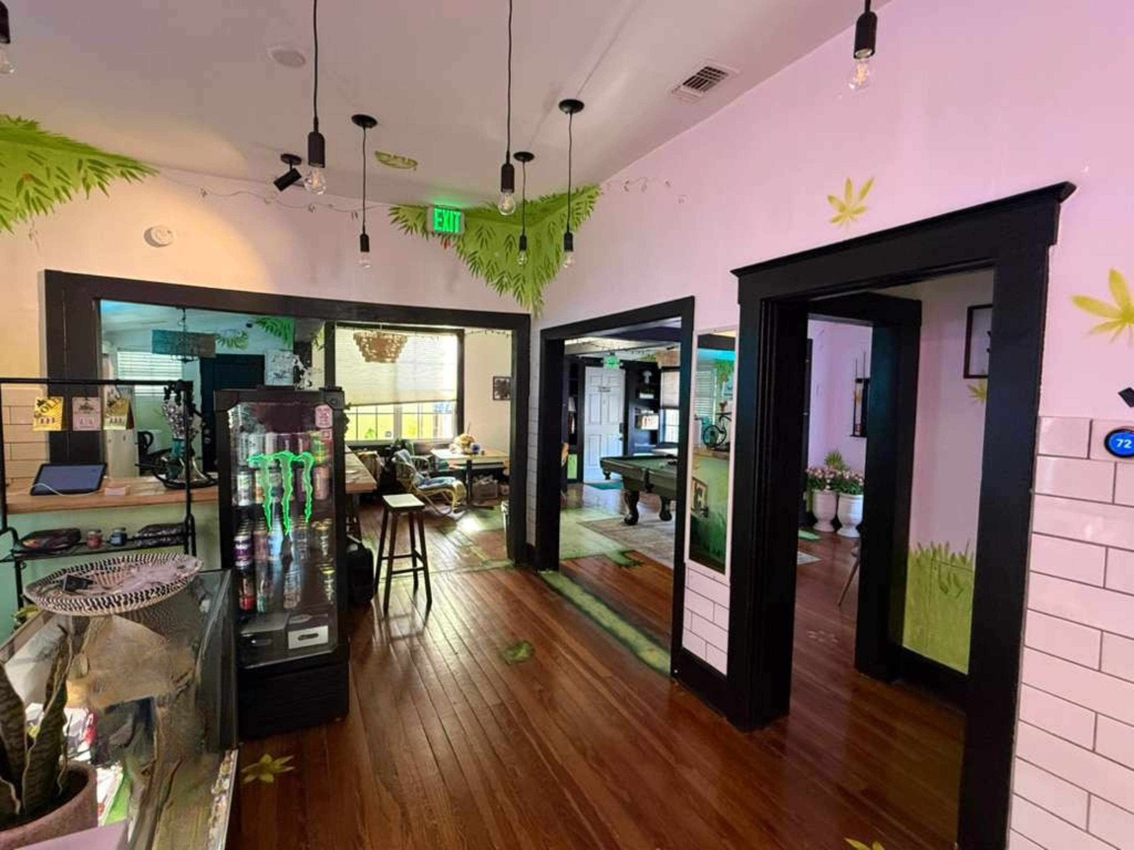 The image shows a brightly lit interior of a business with decorative green plants painted on the walls, a display fridge, and a pool table in the background.
