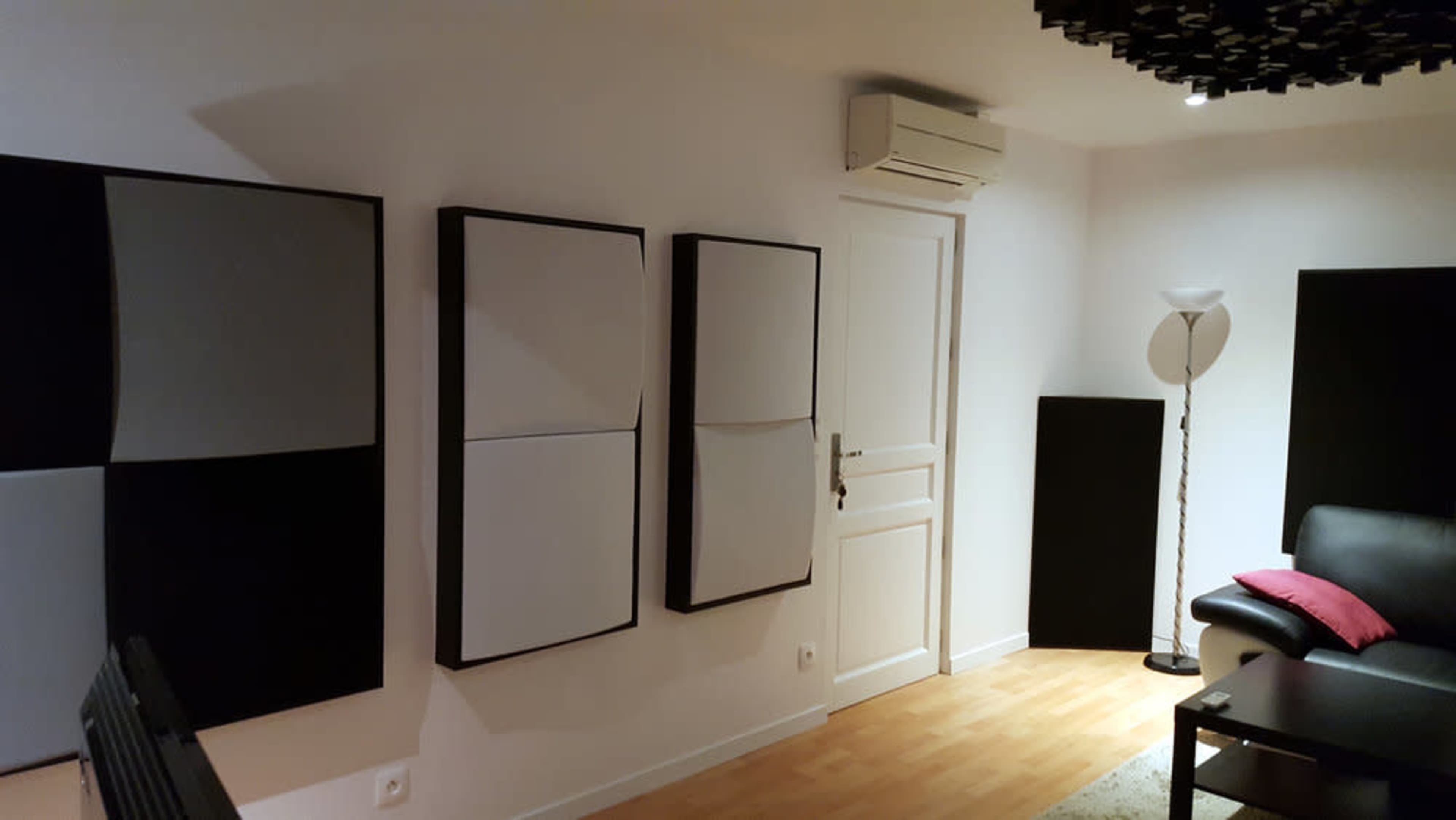 A modern room featuring a black leather sofa, a lamp, and several sound-absorbing panels mounted on the walls.