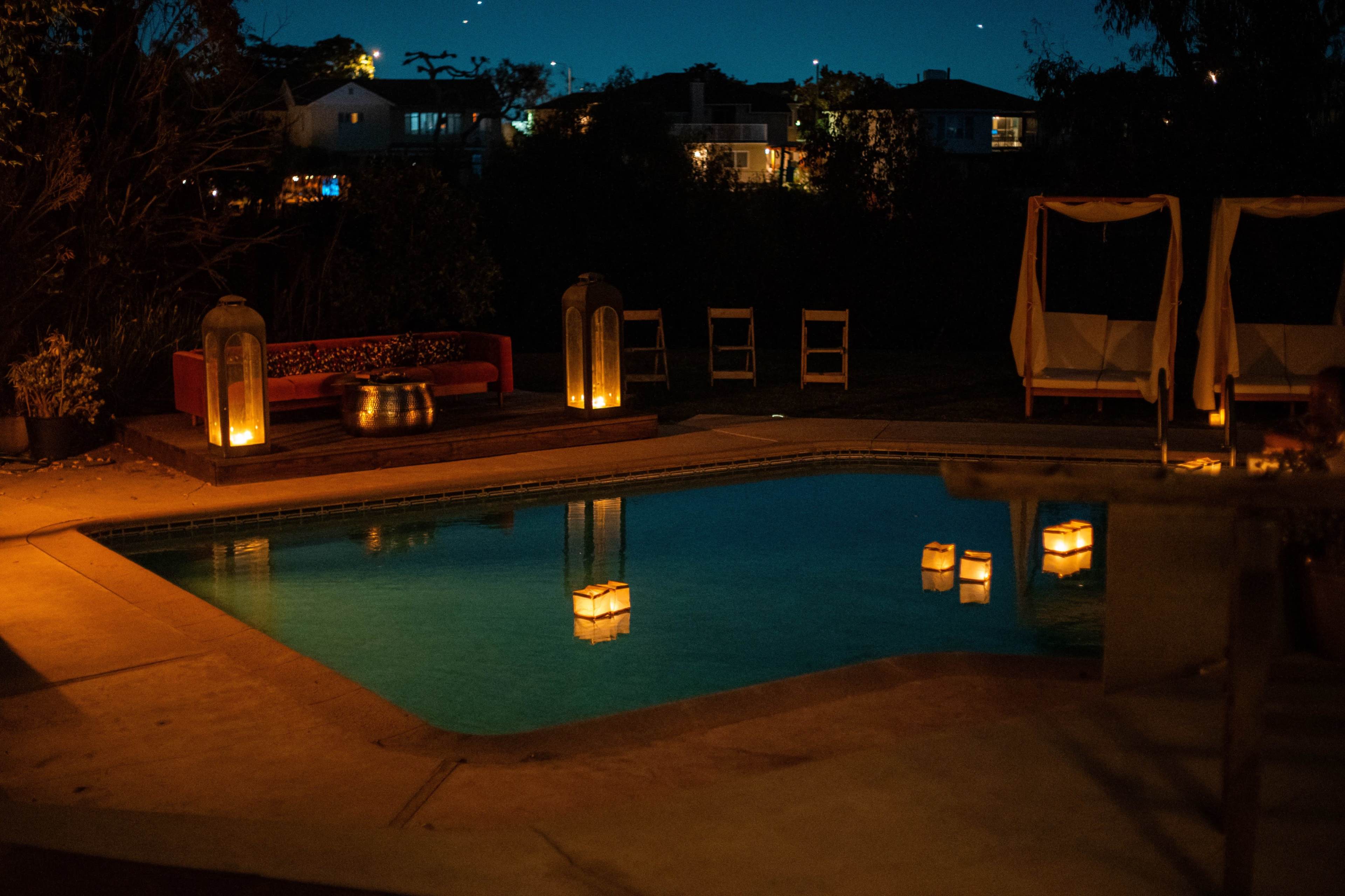 The scene features a dimly lit pool area with floating lanterns, a red sofa, and illuminated lanterns surrounding the pool.