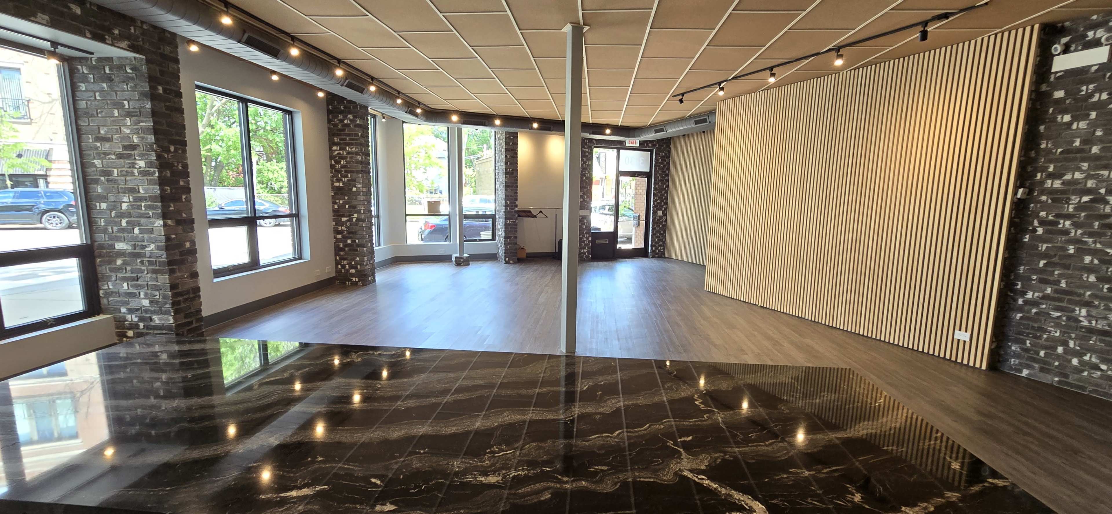 An empty commercial space with large windows, wooden paneling, and a polished black and white marble floor.
