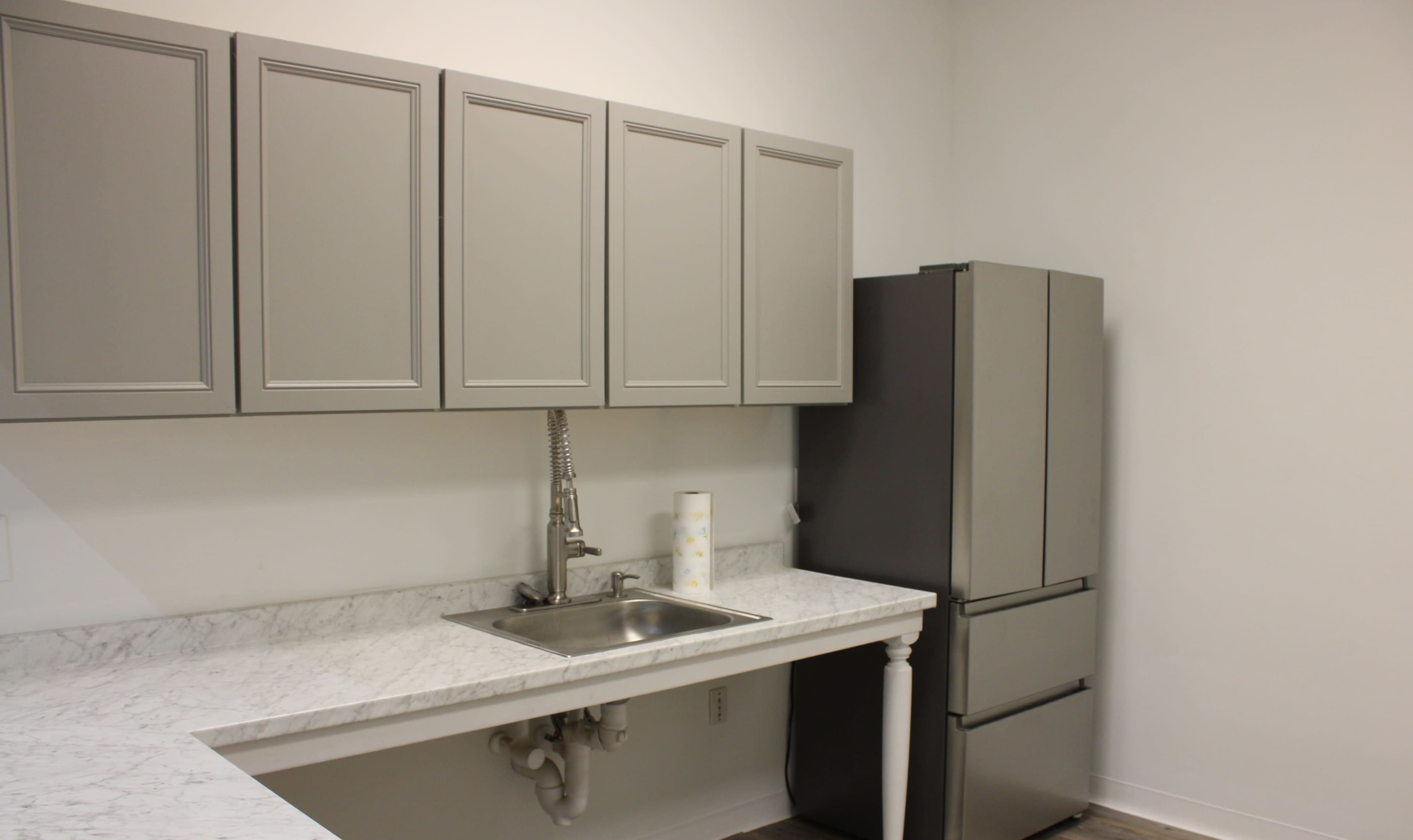 A modern kitchen with gray cabinets, a marble countertop, a stainless steel sink, and a matching refrigerator.