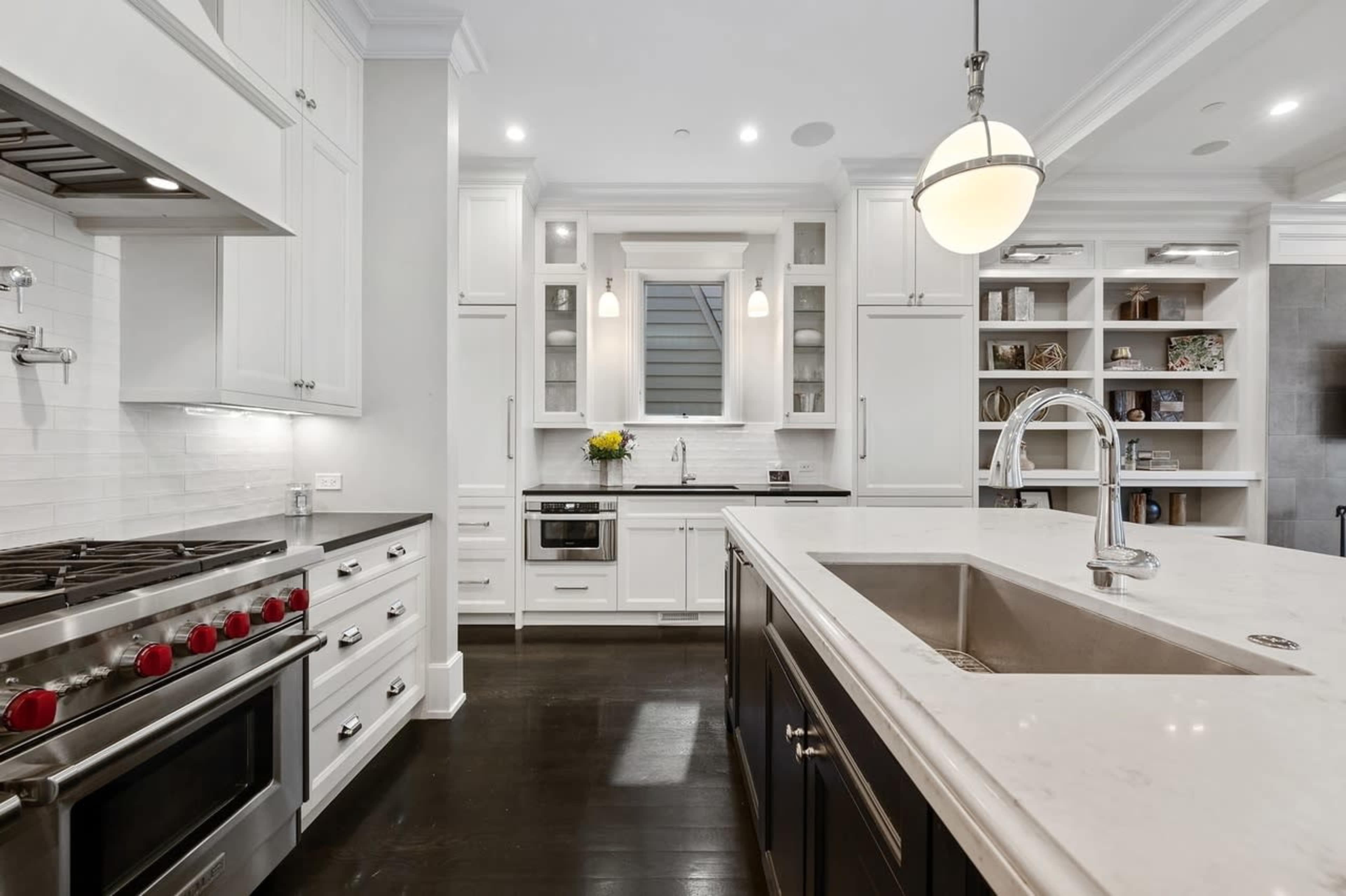 A modern kitchen features white cabinetry, stainless steel appliances, and a large island with a stainless steel sink.