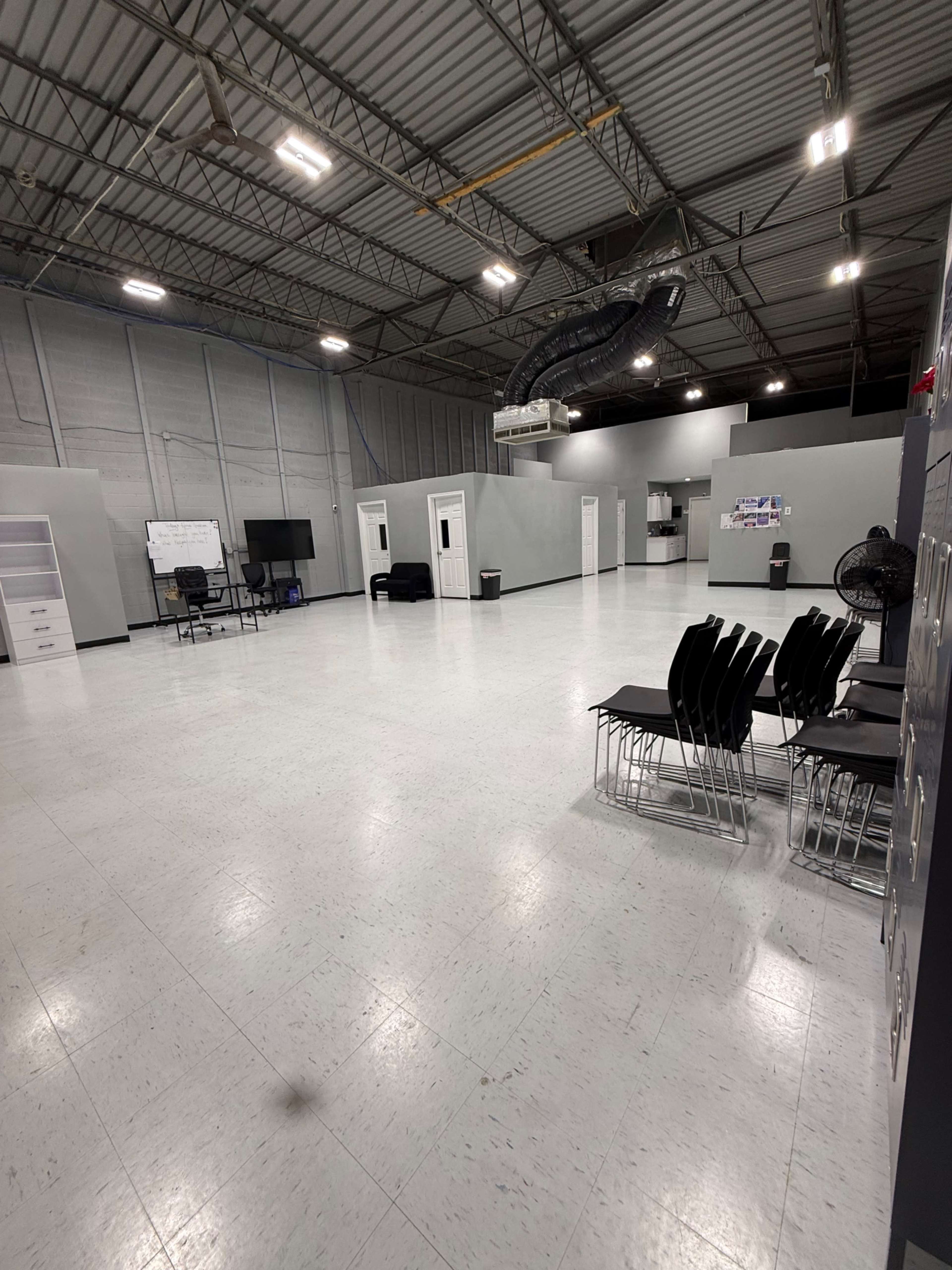 The image shows a spacious, empty room with gray walls, a few pieces of furniture, and a shiny floor.