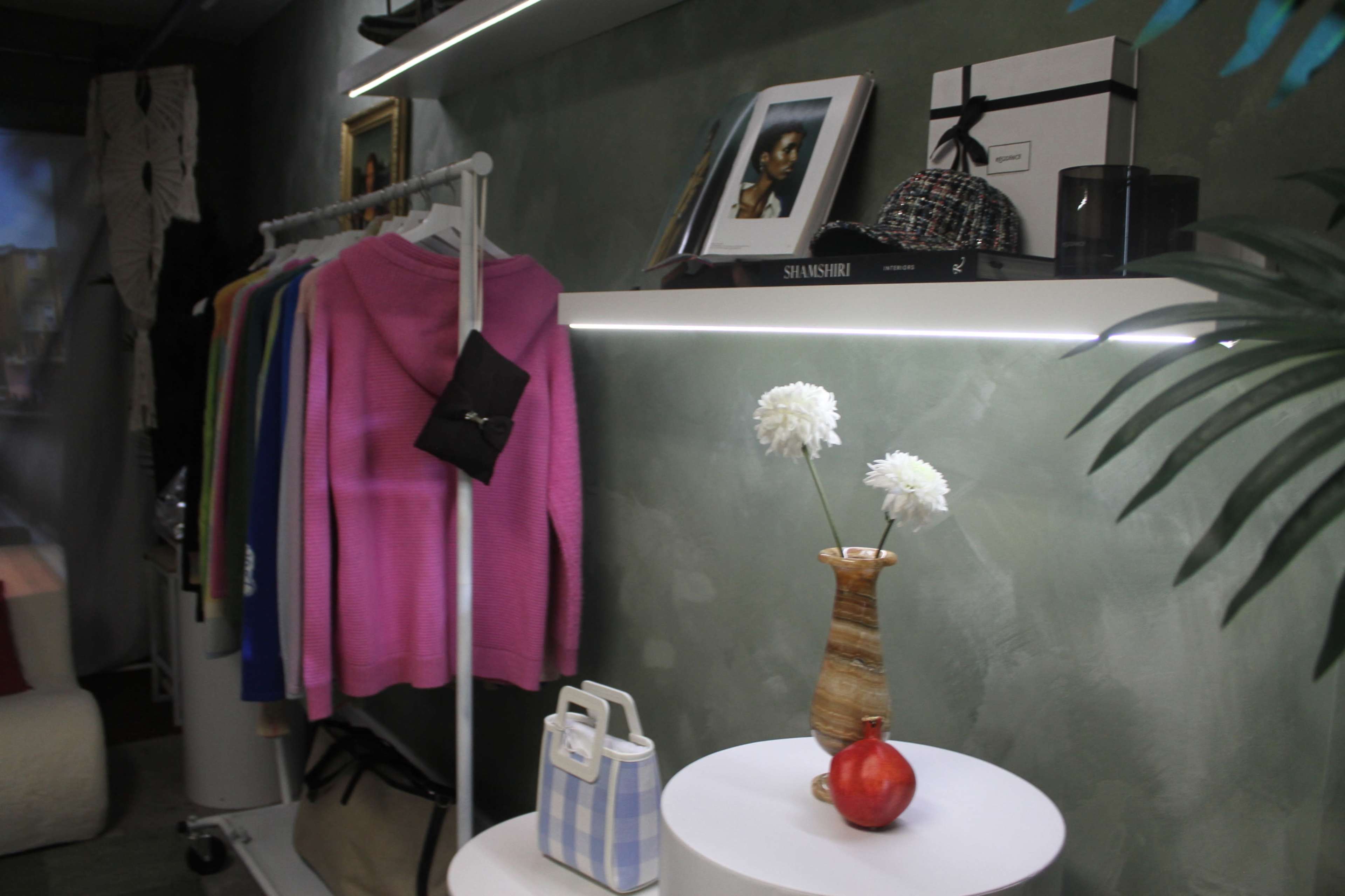 A clothing display features colorful sweaters on a rack beside a shelf with decorative items, including flowers in a vase and a small fruit.