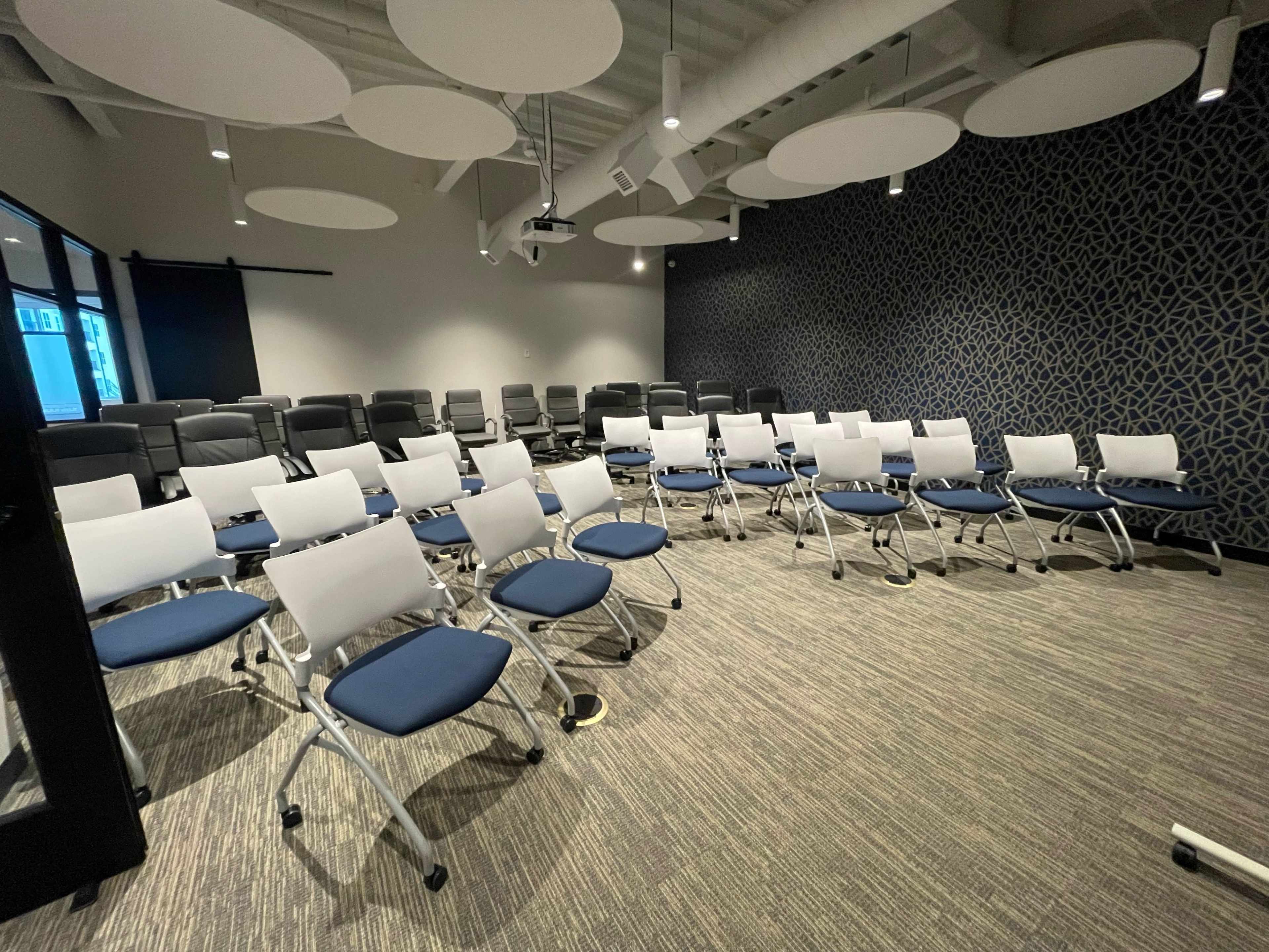 A meeting room set up with rows of blue and white folding chairs facing a projection screen.