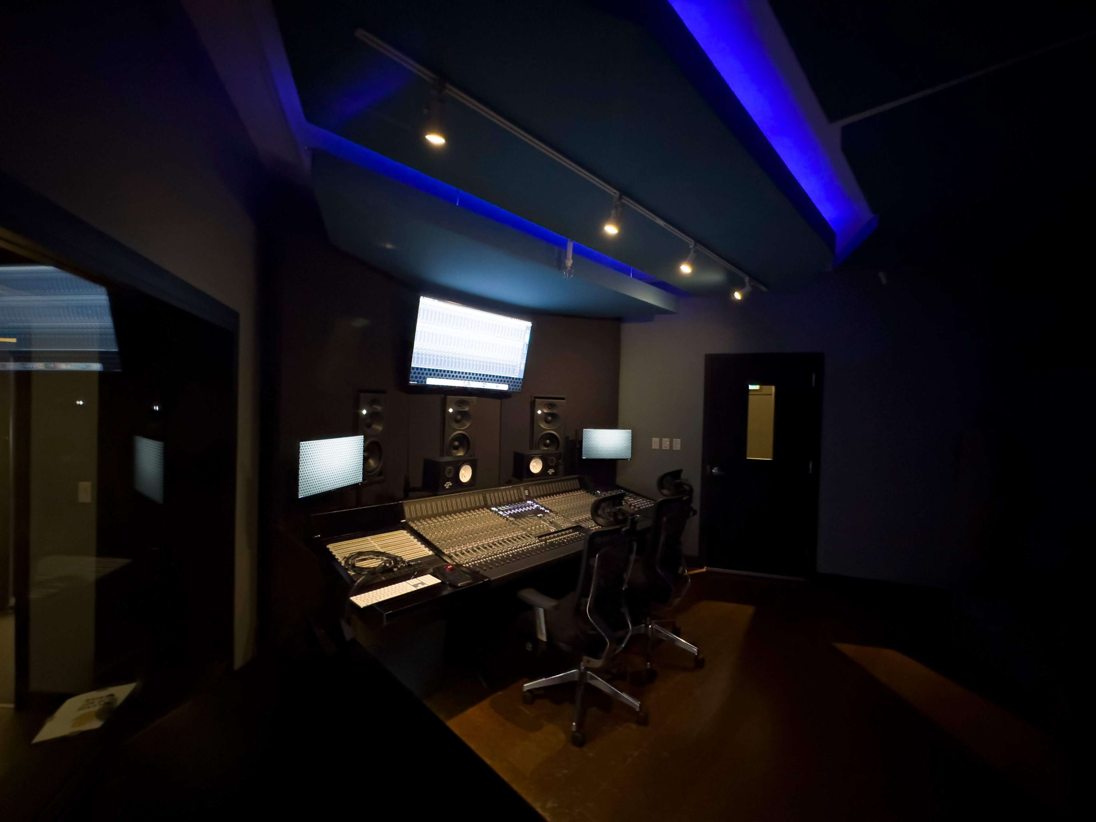 A recording studio with a control desk, speakers, and two office chairs in a dimly lit space.