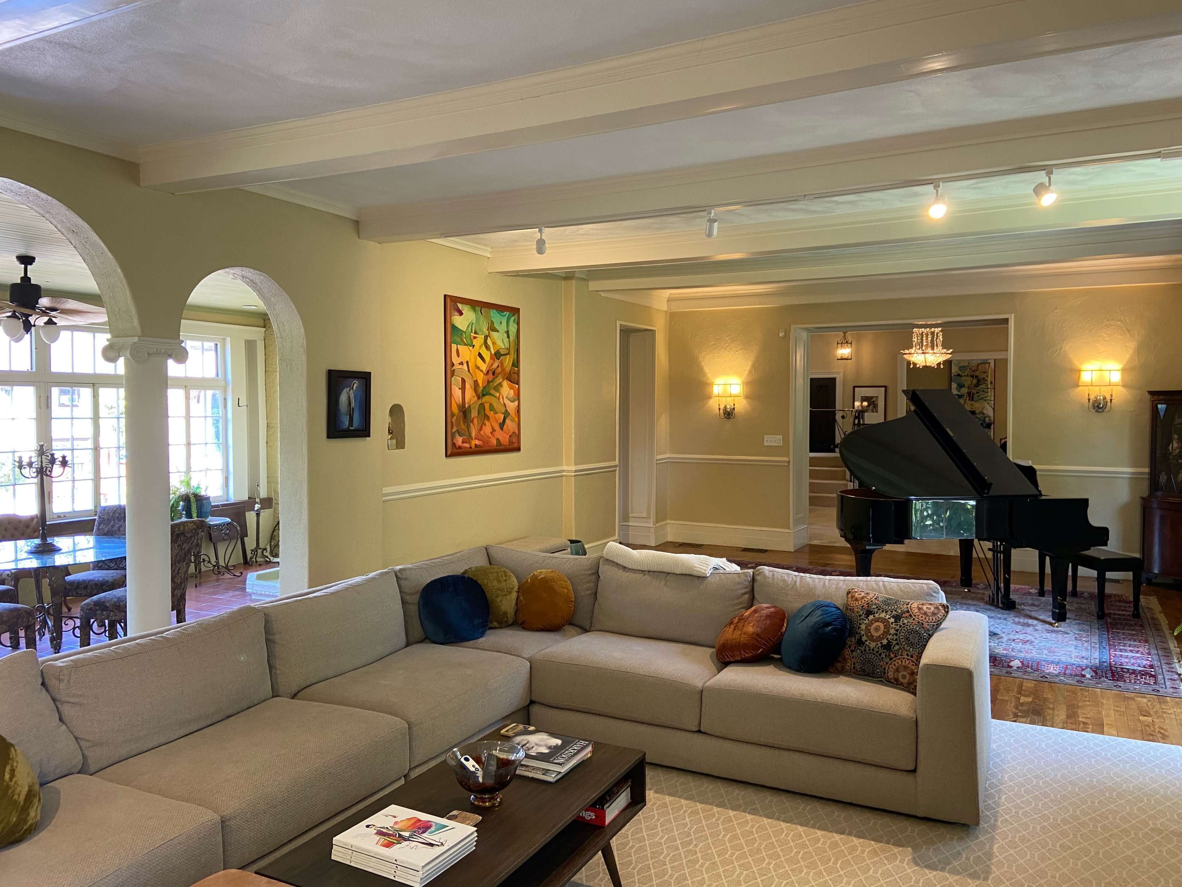 A spacious living room with a large sectional sofa, a coffee table, an art piece on the wall, and a grand piano in the adjoining area.