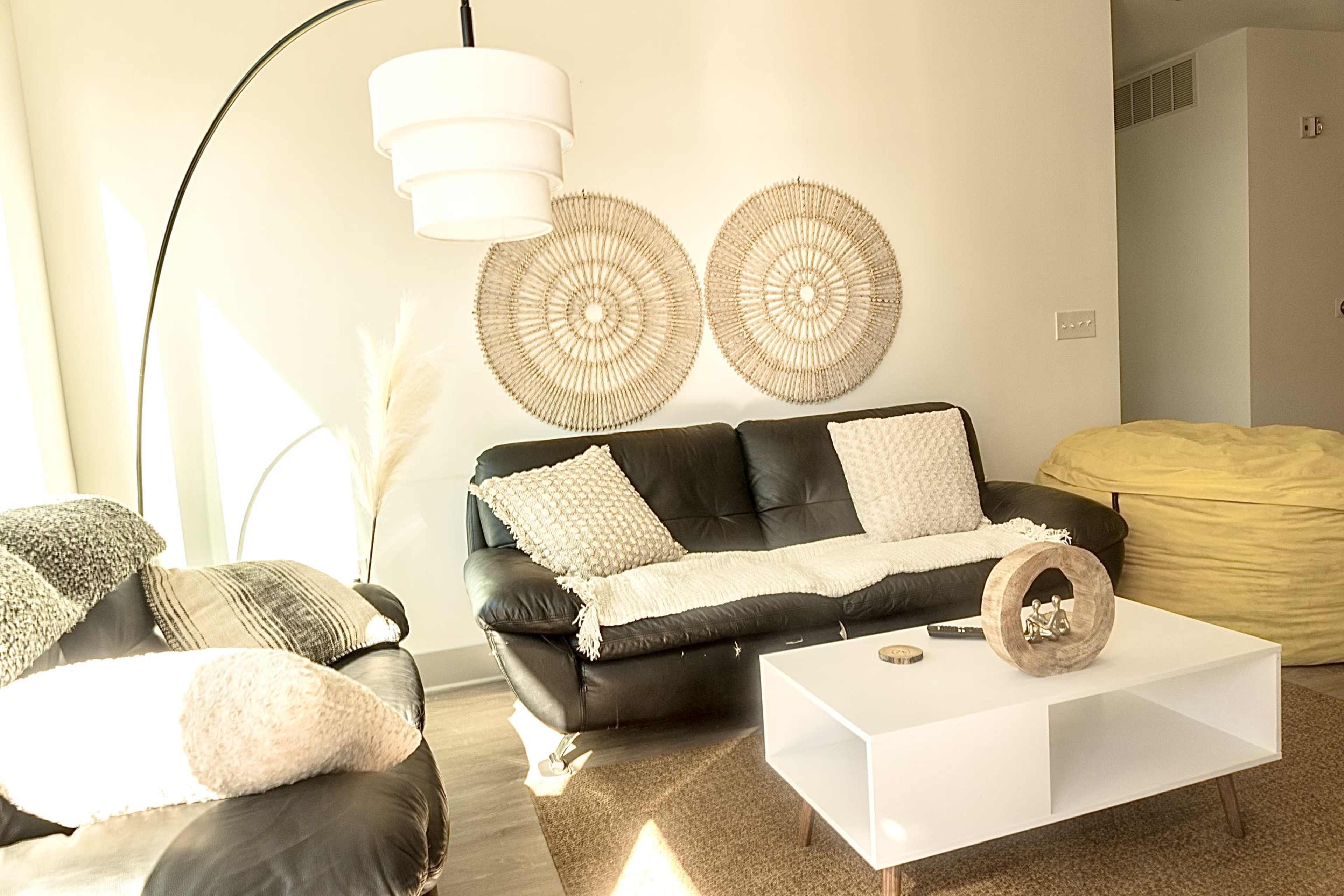 A living room with a black sofa, a white coffee table, decorative wall hangings, and a yellow bean bag chair.