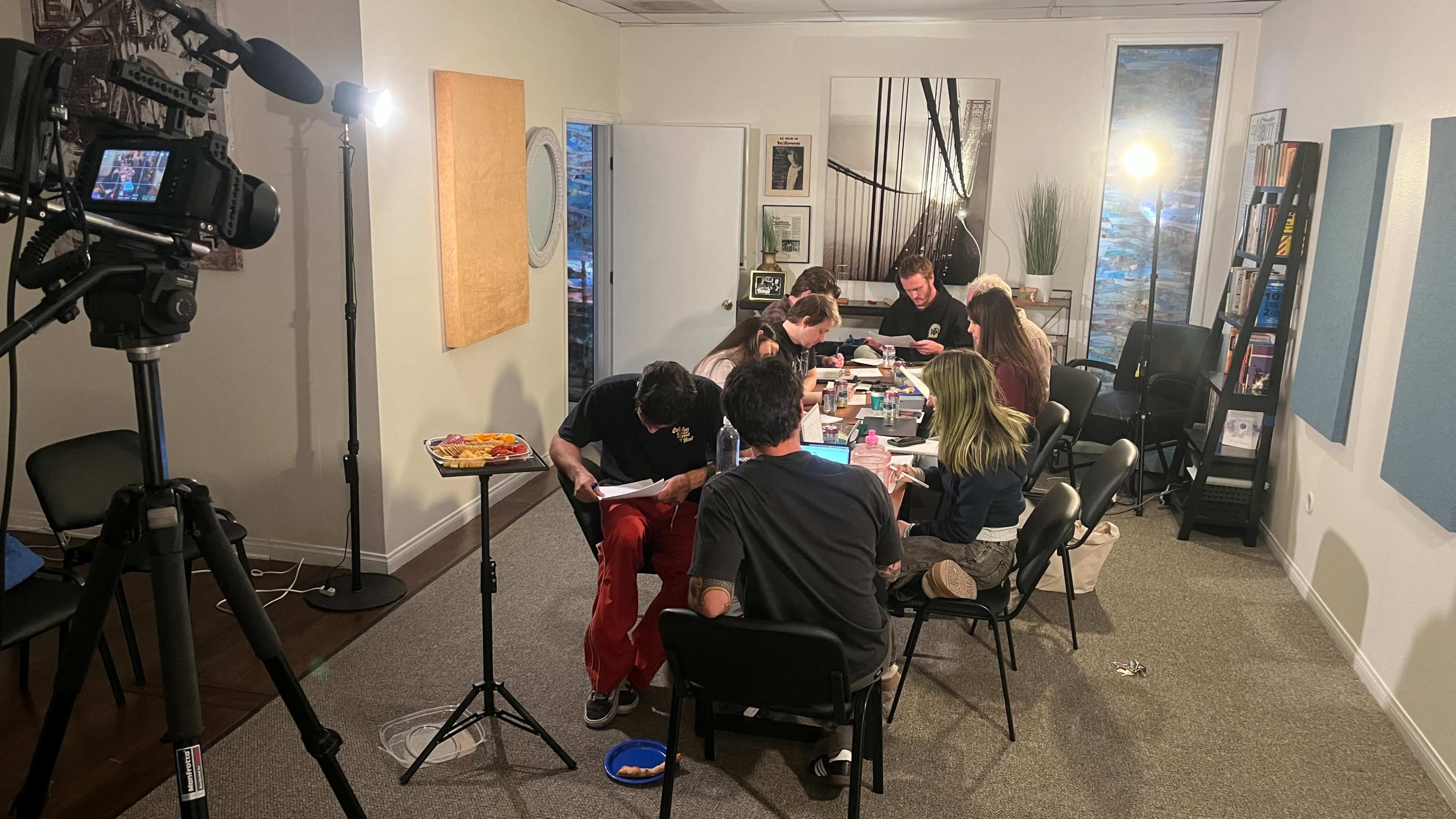 A group of eight people sits around a table covered with papers and materials, engaged in an activity in a well-lit room.