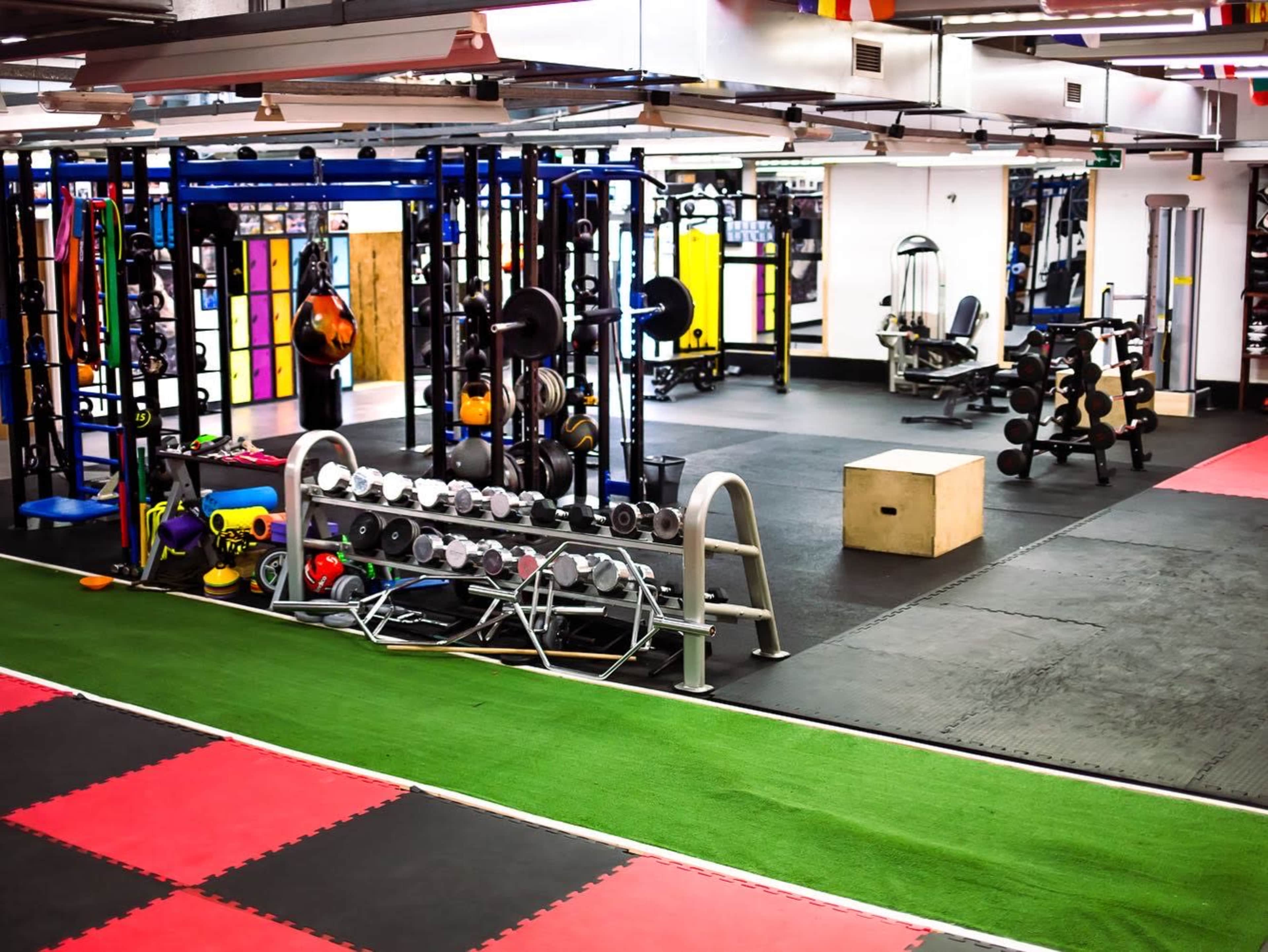 The image shows a gym space featuring workout equipment, including weight racks, exercise bikes, and a plyometric box on a rubber floor.