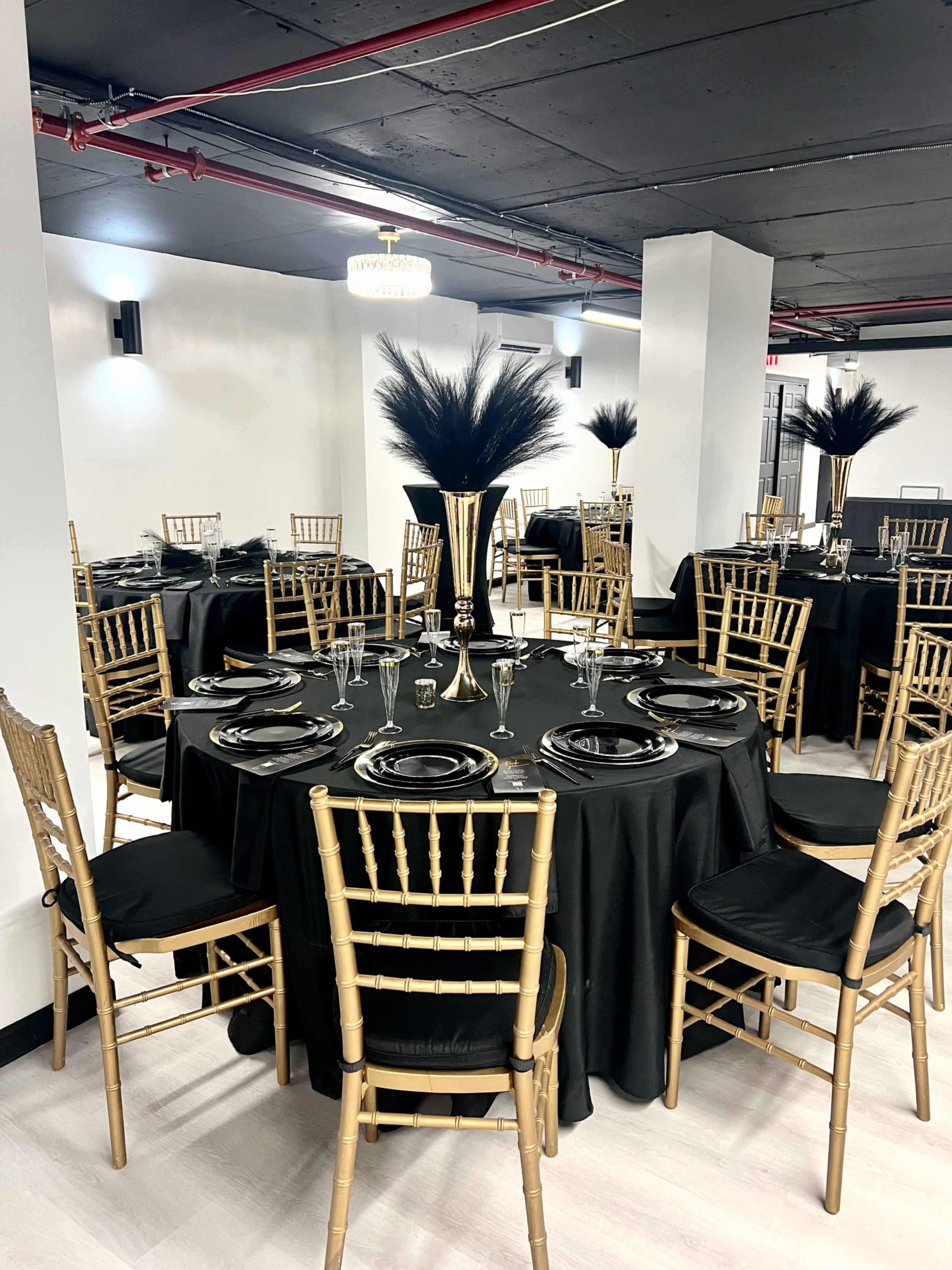A banquet hall set up with round tables covered in black cloth, each adorned with elegant centerpieces and gold chiavari chairs.