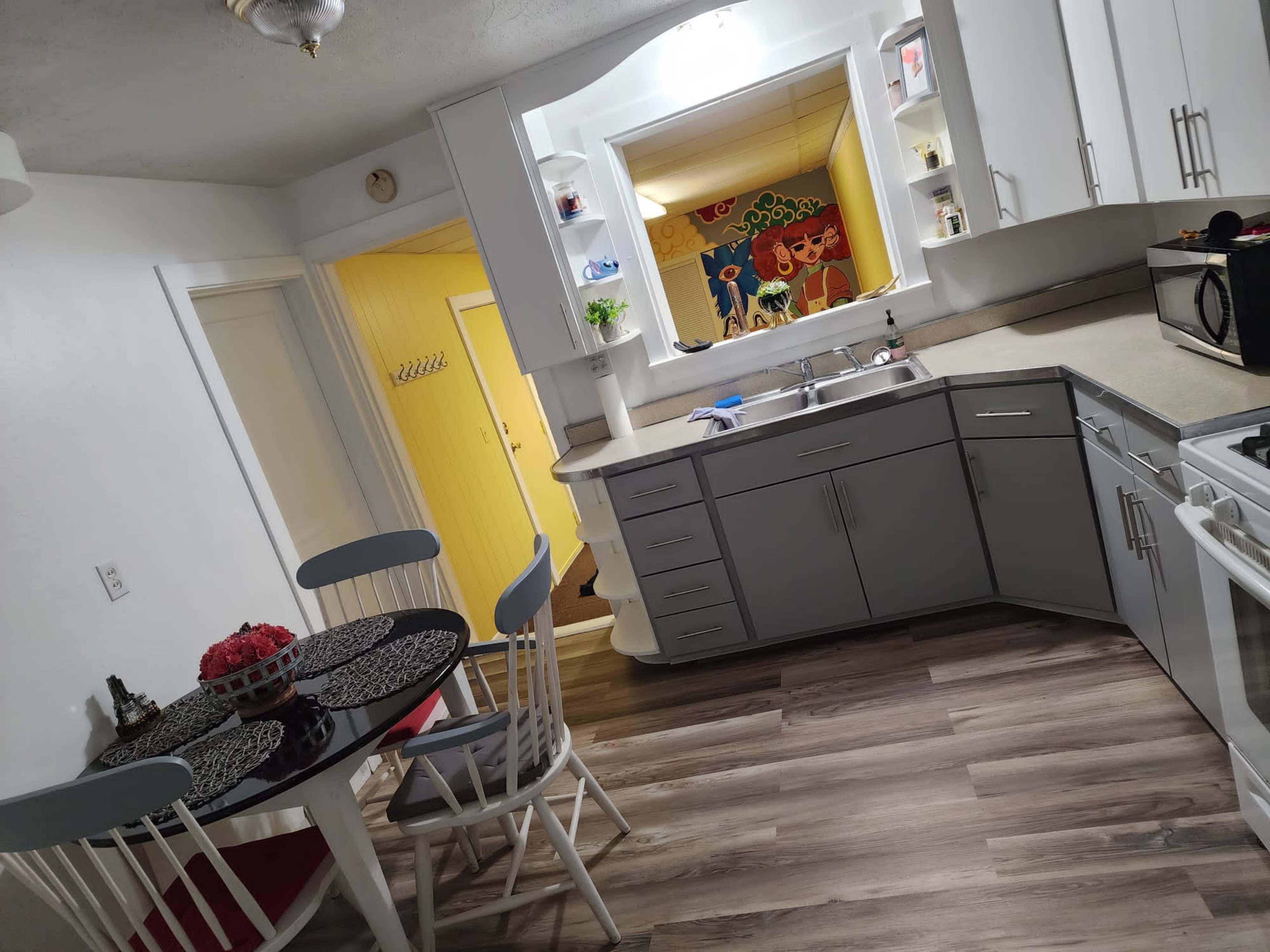 A modern kitchen with gray cabinets, a round dining table, and an open doorway leading to a brightly colored room.