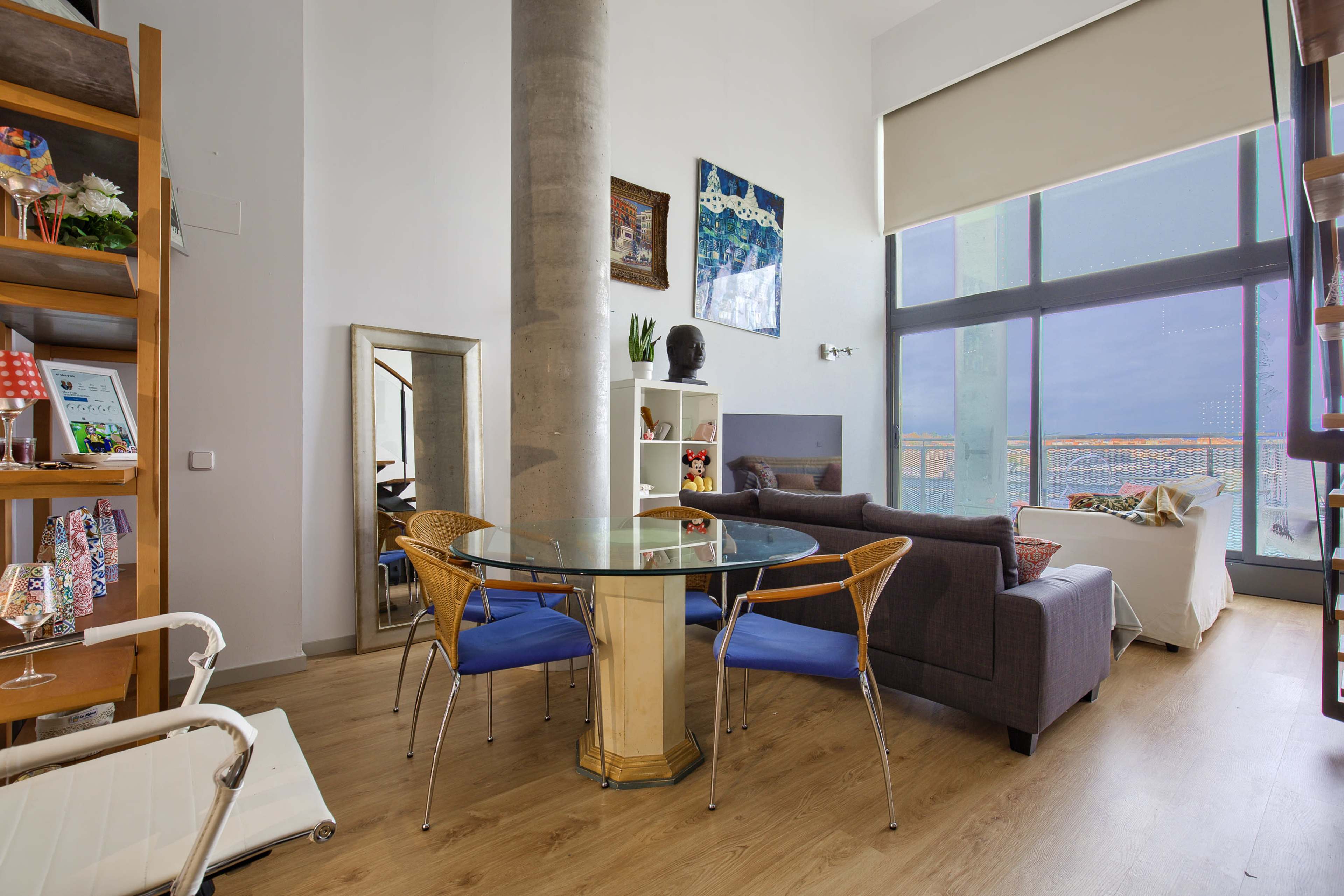 A modern living space featuring a round glass dining table with four chairs, a cozy couch, and large windows providing a view of the outdoors.