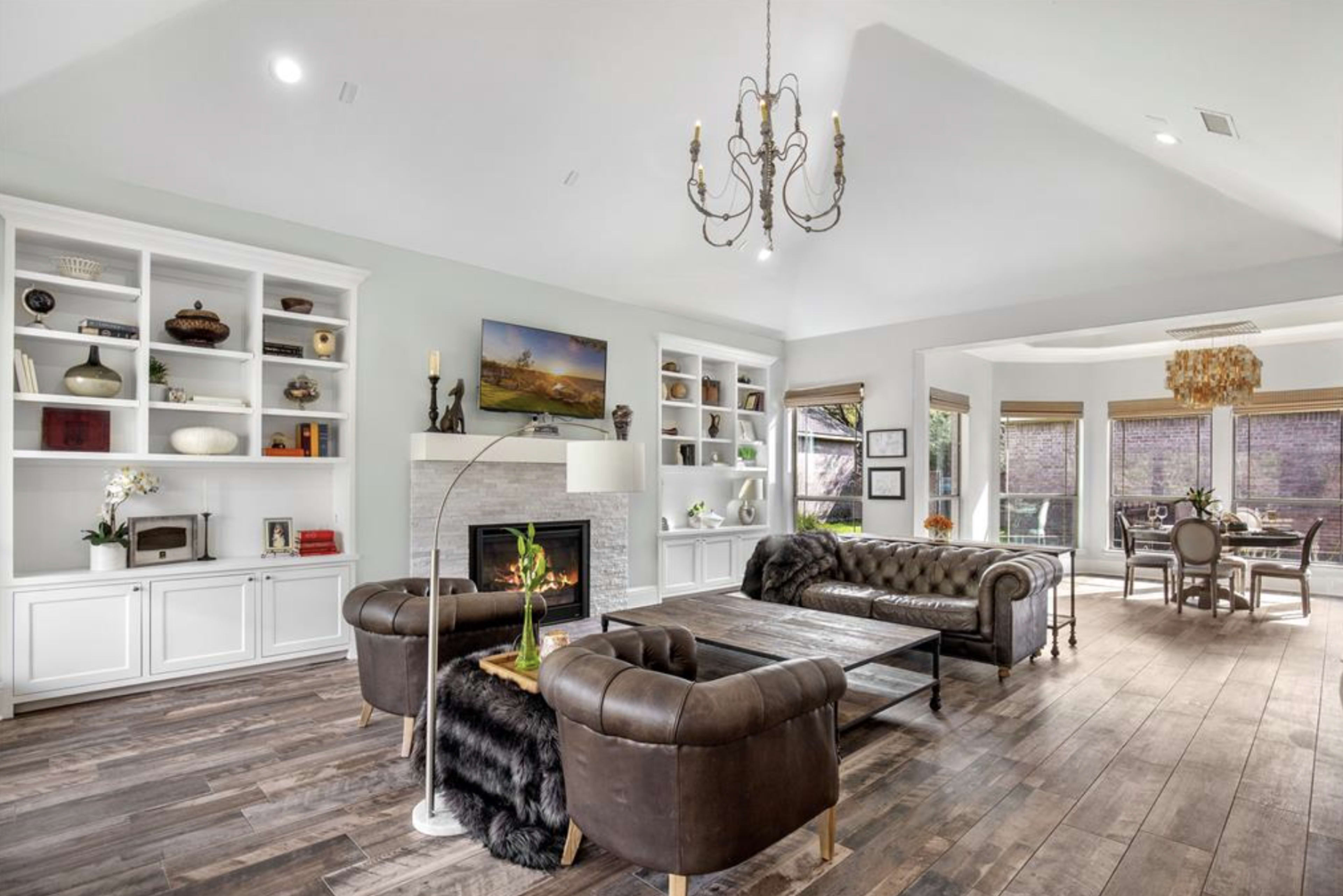 The image shows a spacious living room featuring a leather sofa, wooden flooring, and built-in bookshelves filled with decorative items.