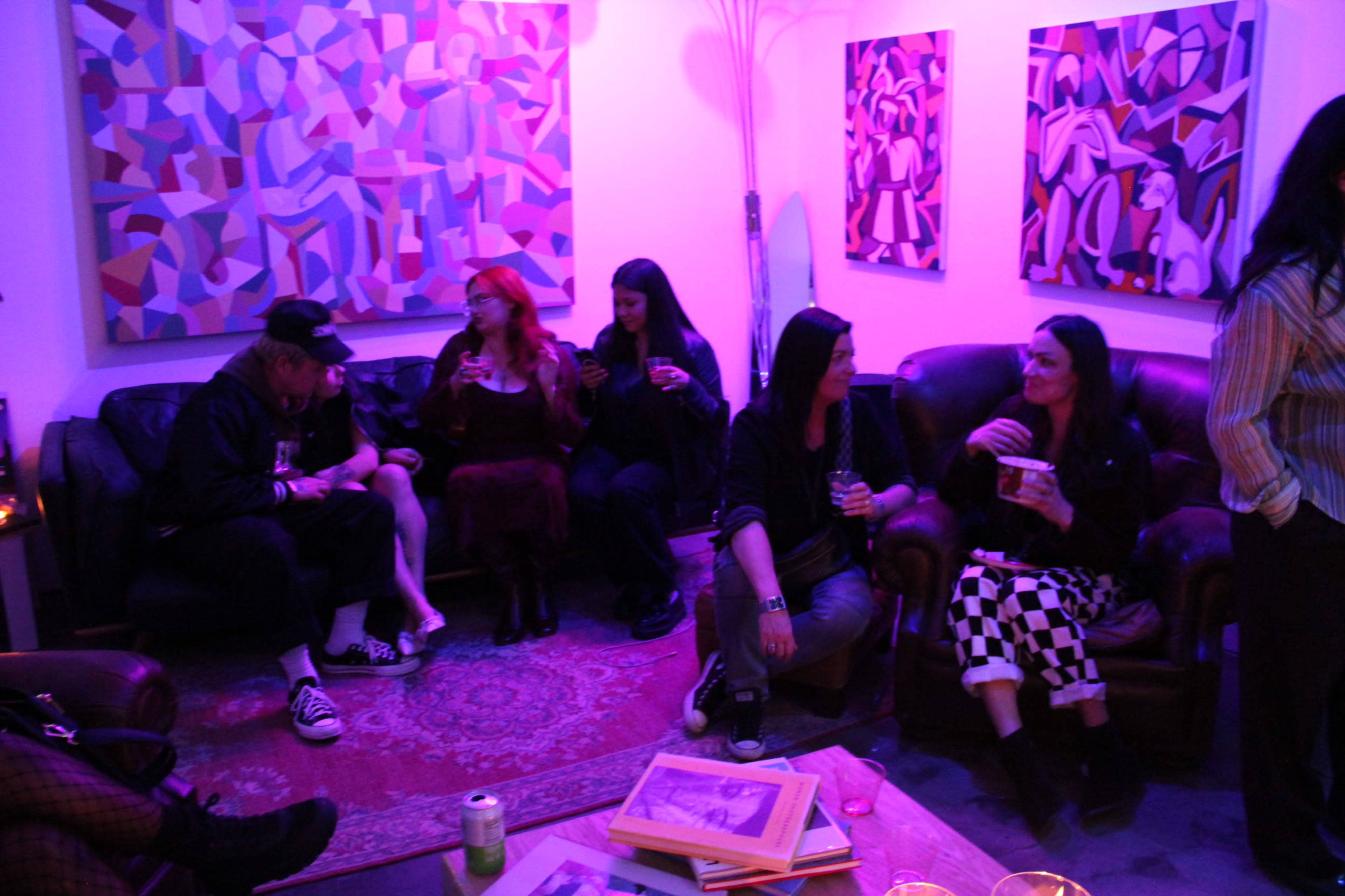 A group of people is sitting on a couch in a dimly lit room decorated with colorful abstract art.