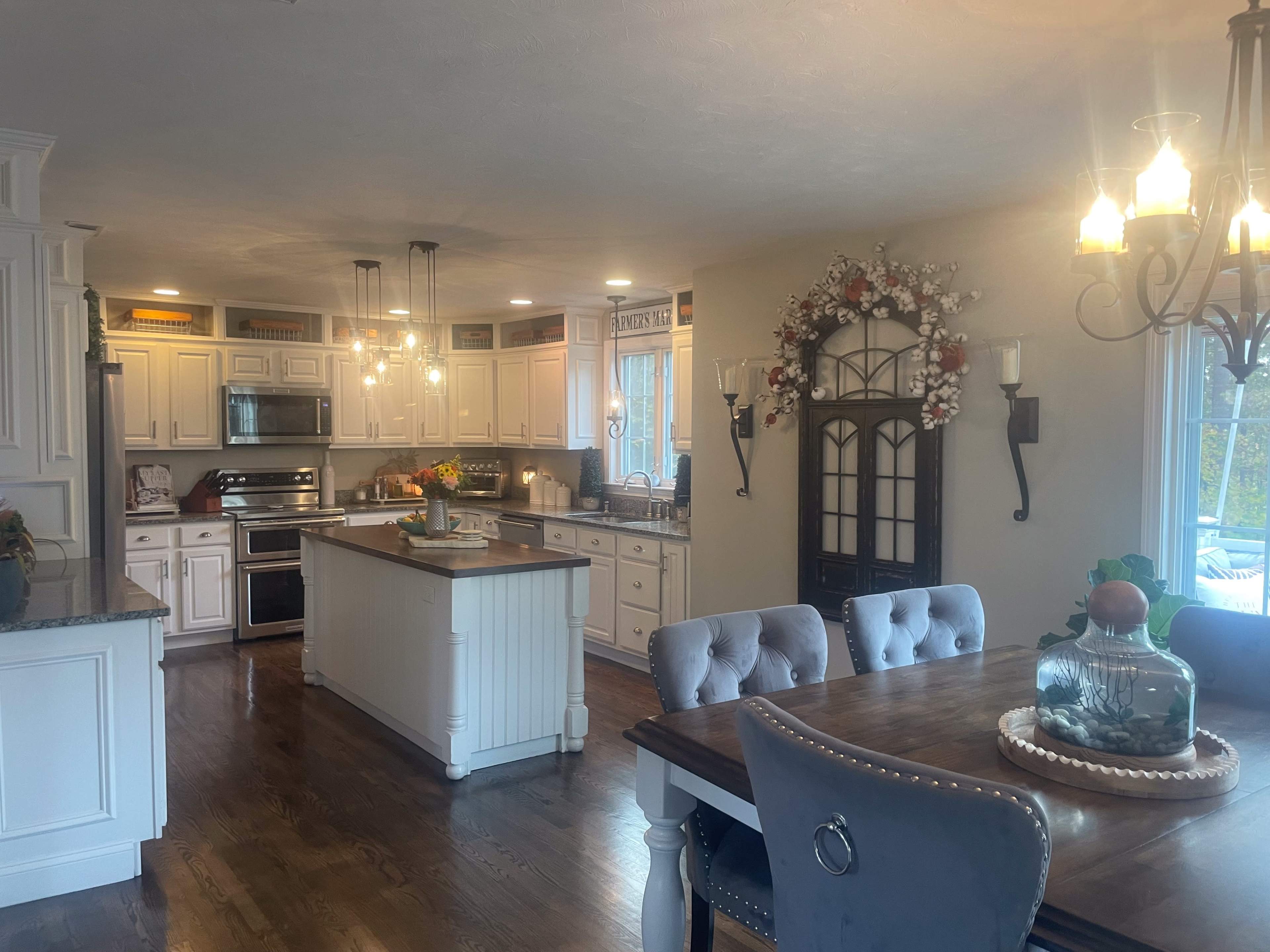 A spacious kitchen with white cabinetry, a central island, and a dining area featuring a wooden table and upholstered chairs.