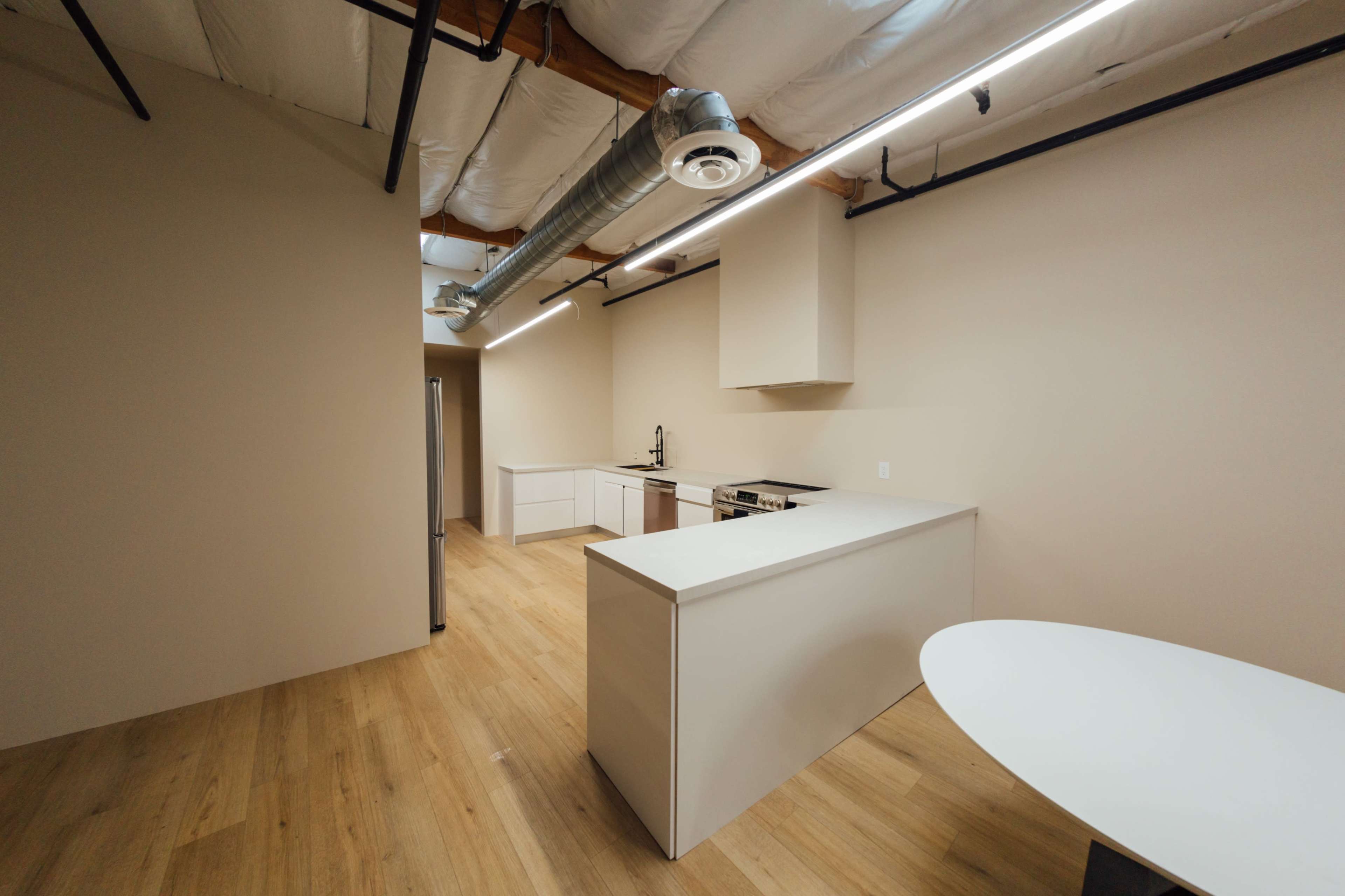 A modern kitchen space with white cabinetry, stainless steel appliances, a large countertop, and wooden flooring.