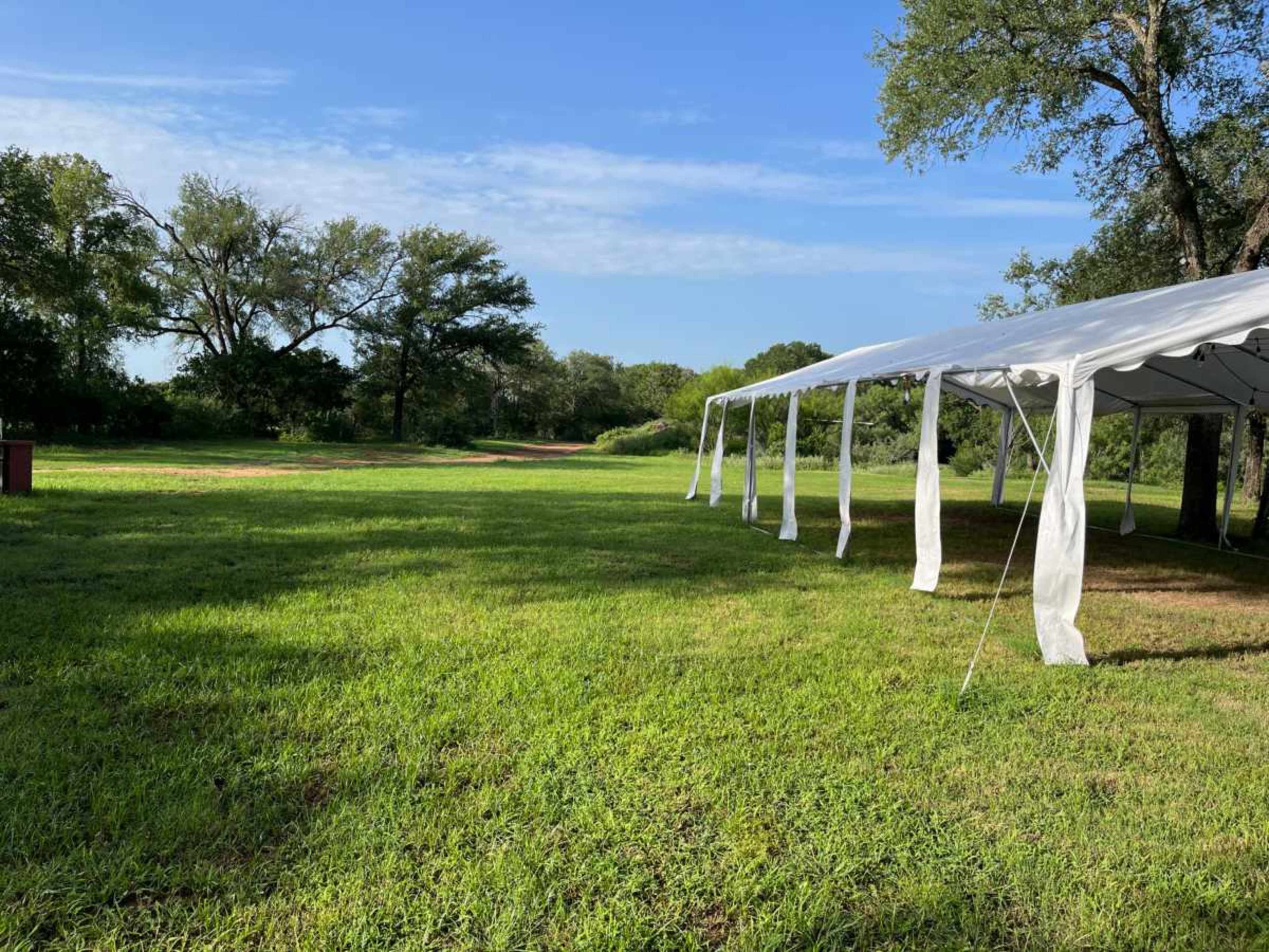A large white tent is set up on a grassy field surrounded by trees under a clear blue sky.