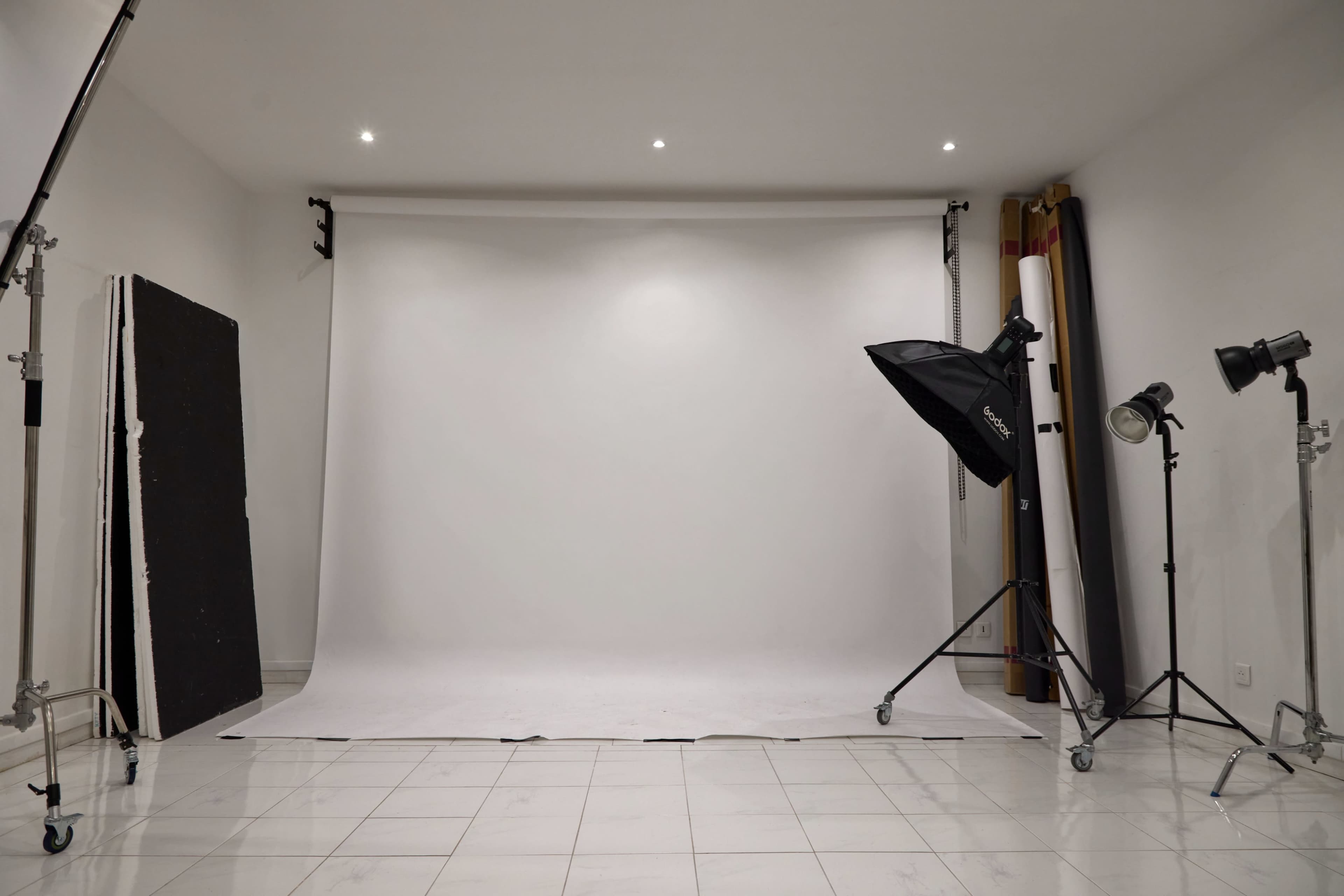 The image shows a photography studio with a white backdrop, studio lights, and a clean tiled floor.