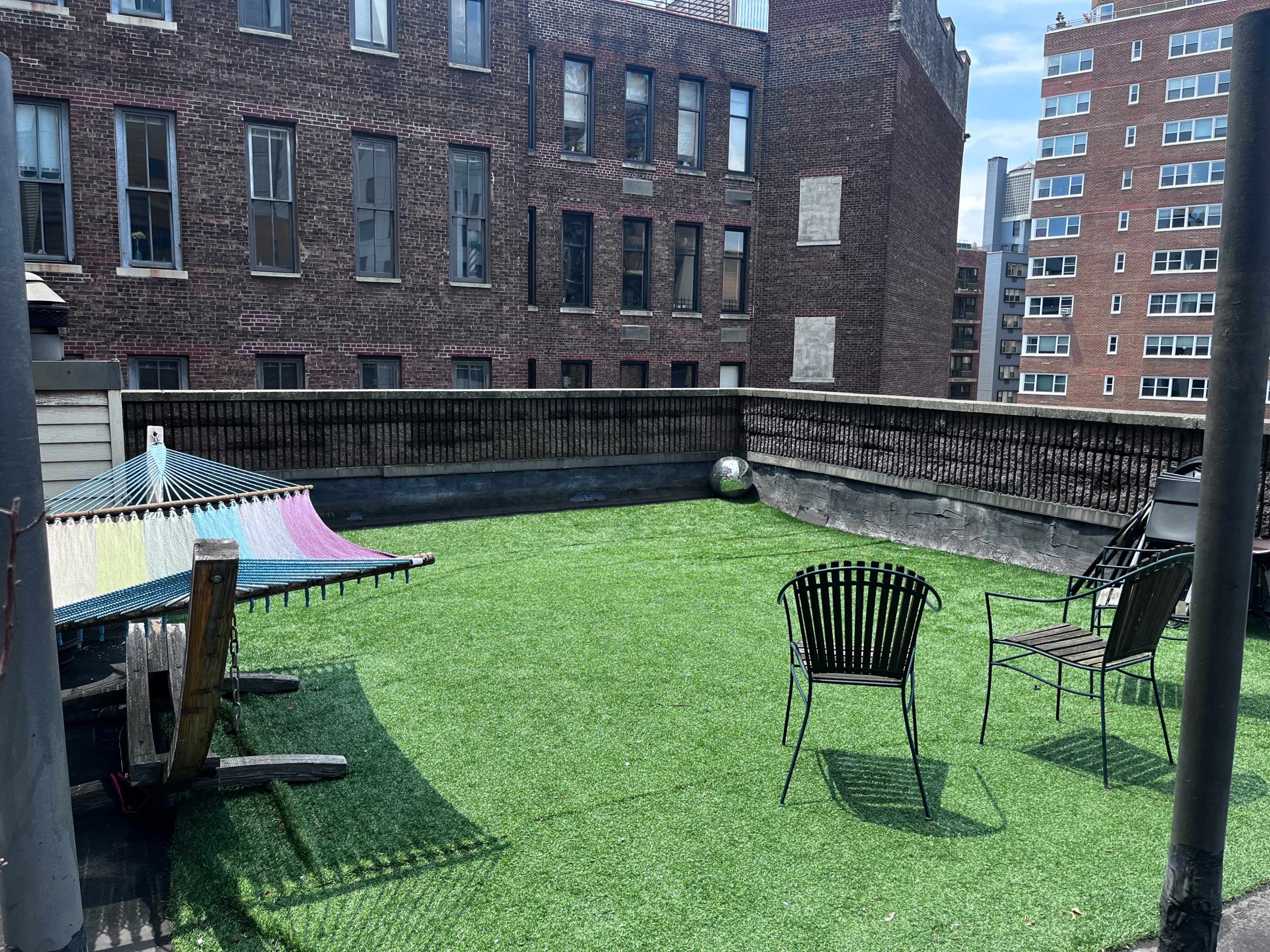 A rooftop terrace with artificial grass, featuring a colorful hammock and two black chairs.