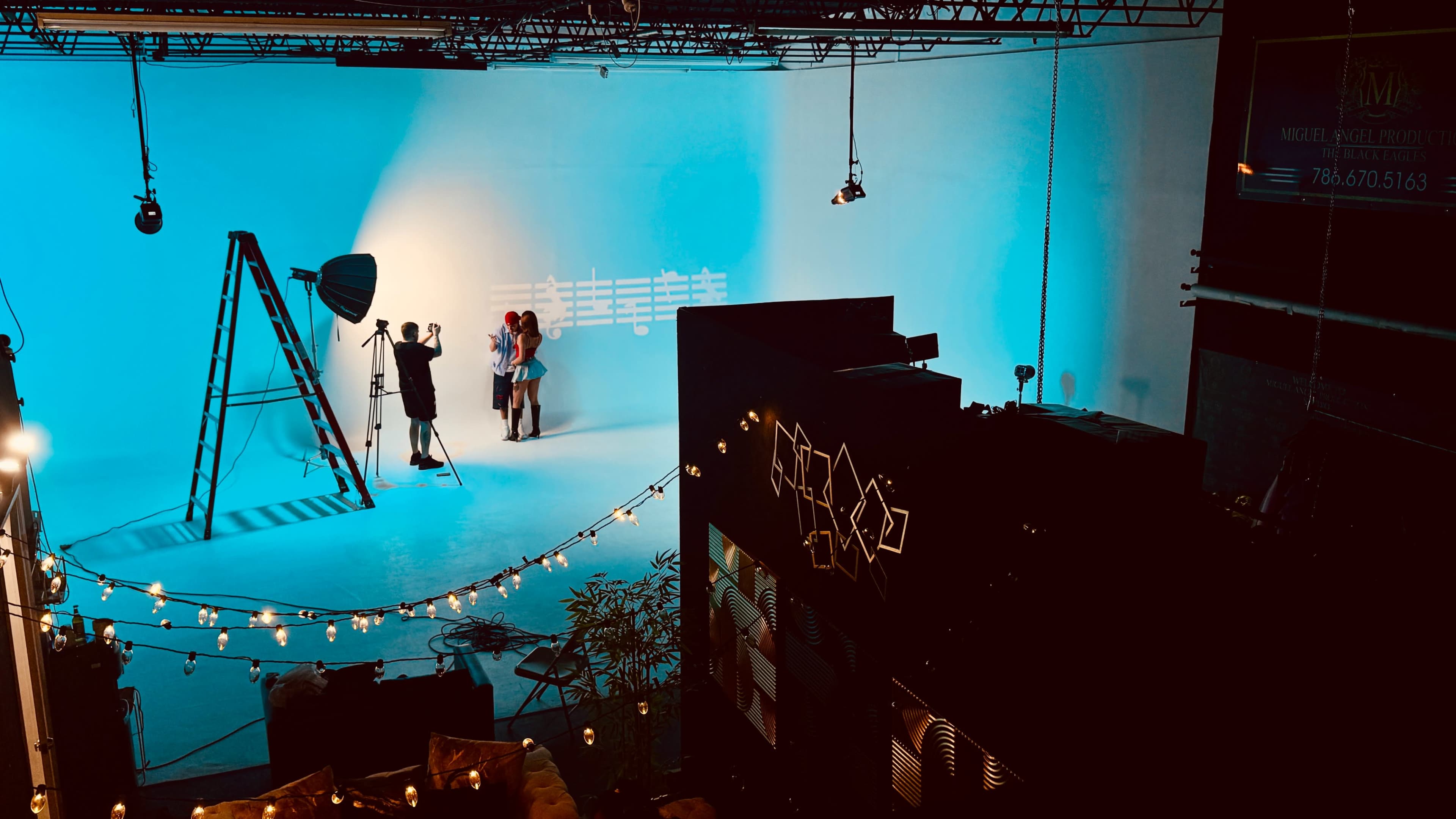 A photographer captures a photo shoot with models in front of a blue backdrop in a studio, illuminated by studio lights.