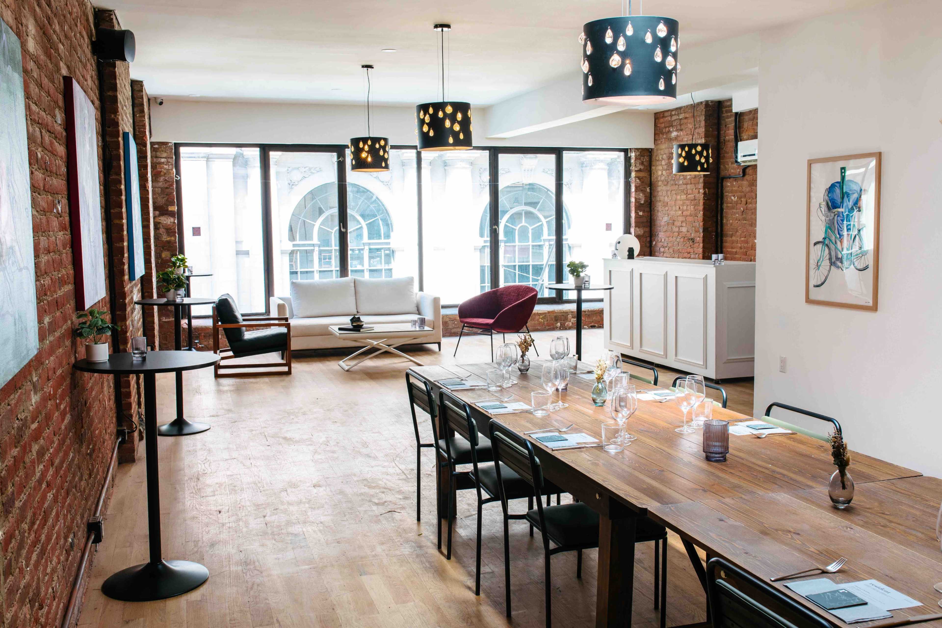 The image shows a modern, open-concept interior featuring a dining area with a wooden table, sleek chairs, and a lounge space with a sofa and armchair, all illuminated by pendant lights.