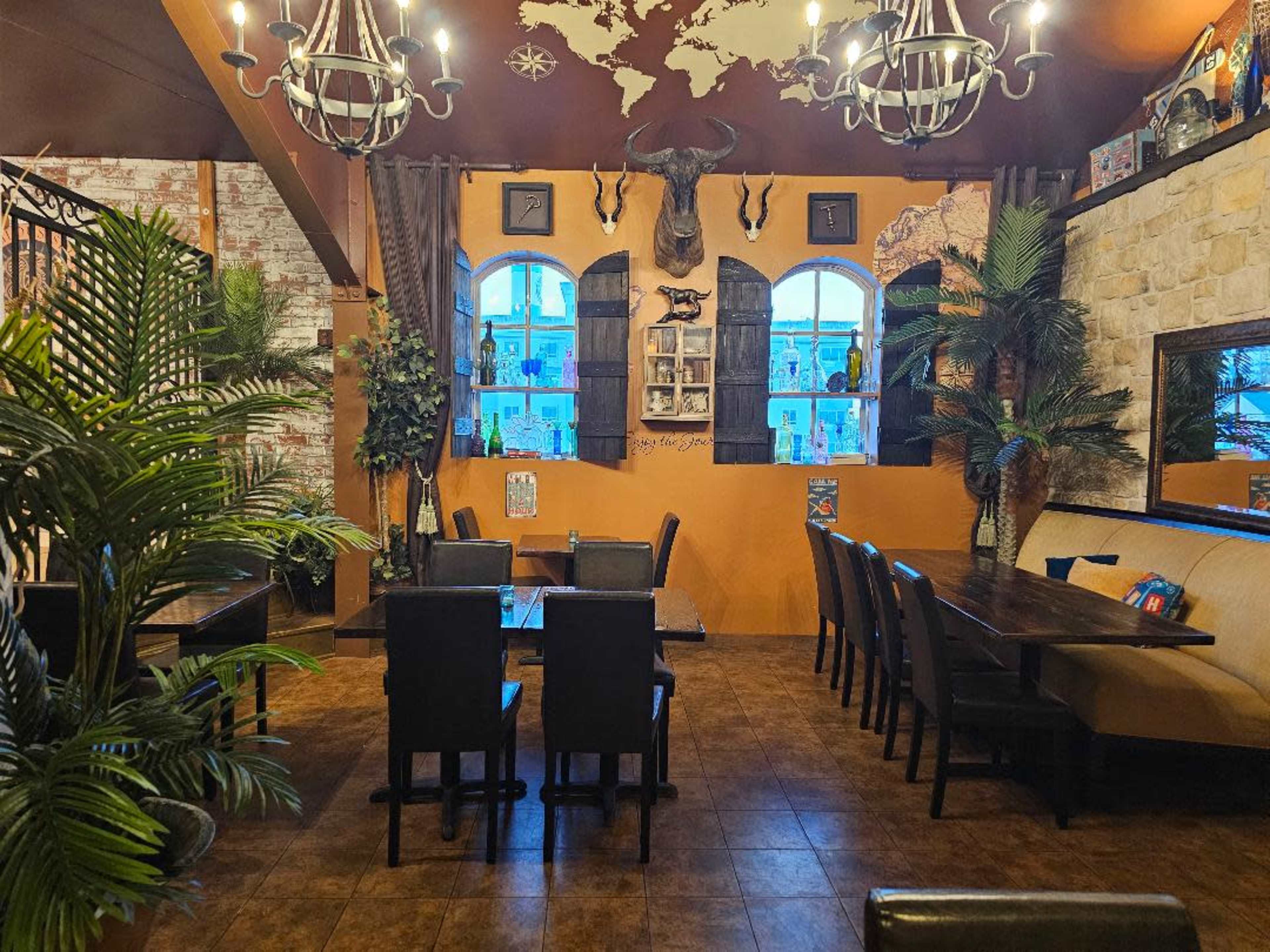 The image shows an inviting restaurant interior with wooden tables, black chairs, plants, and a large map on the wall.
