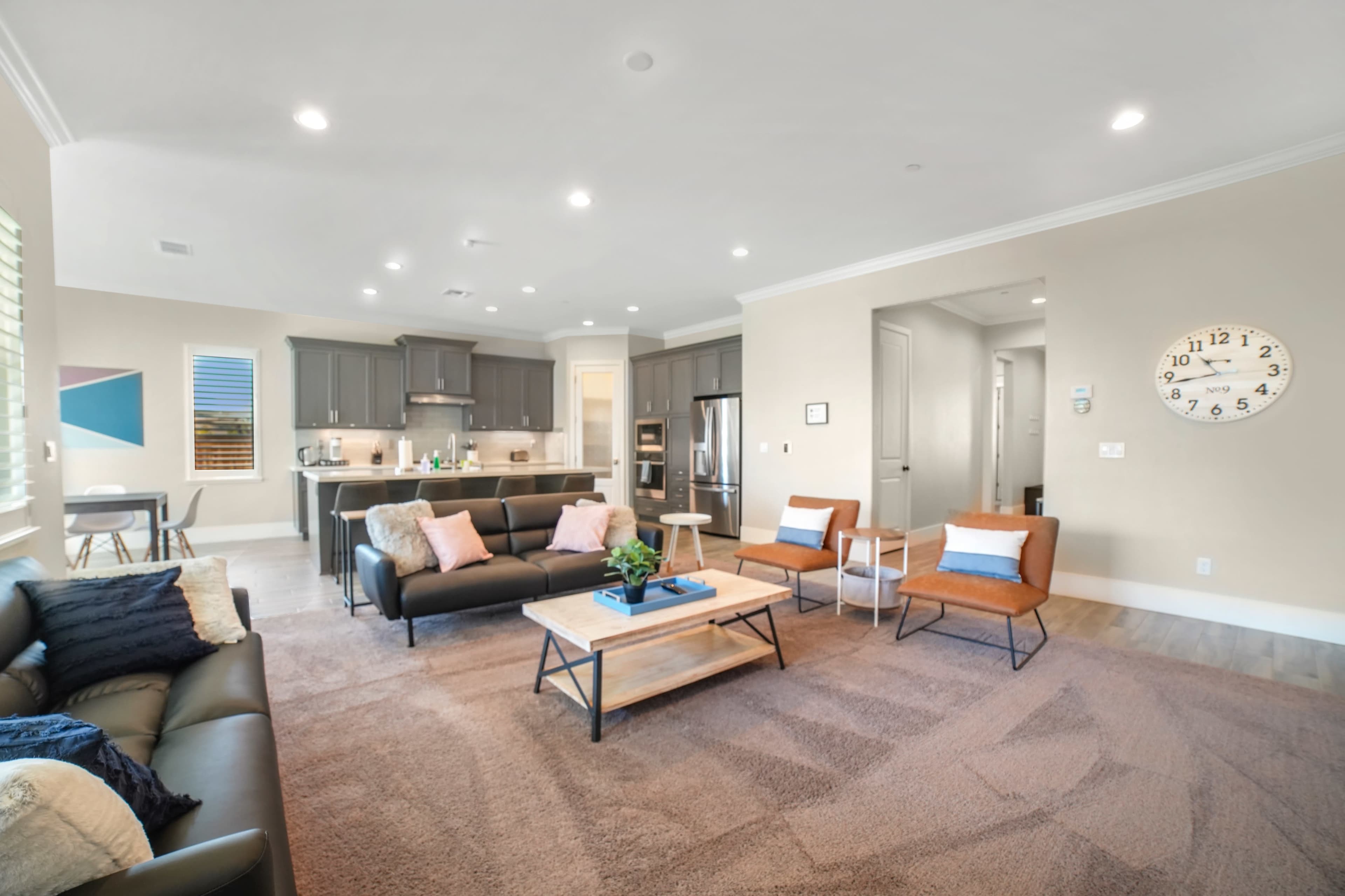 A modern living room with a dark sofa, orange chairs, a coffee table, and a kitchen visible in the background.
