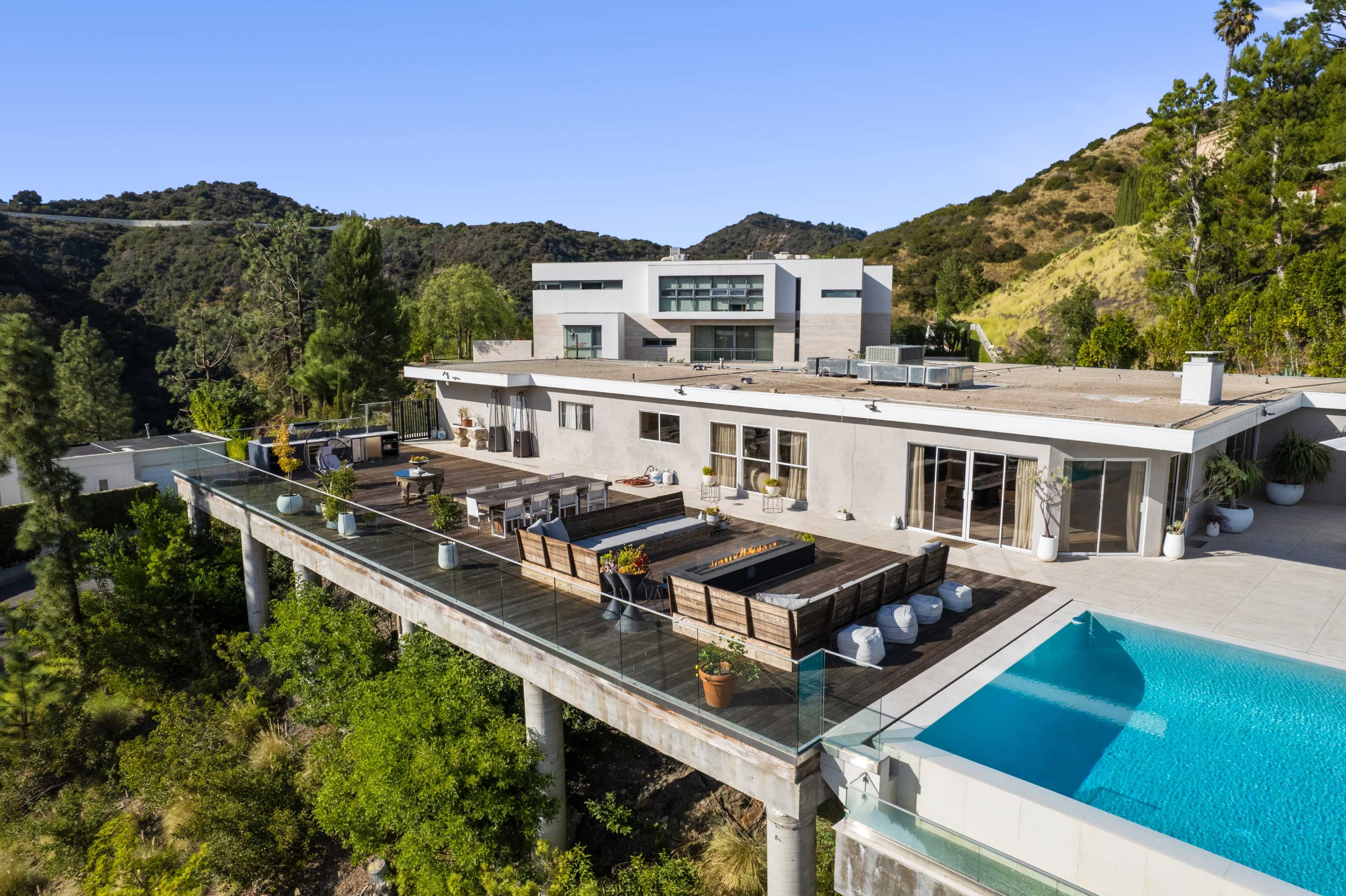 A modern house is situated on stilts overlooking a pool and surrounded by green hills.