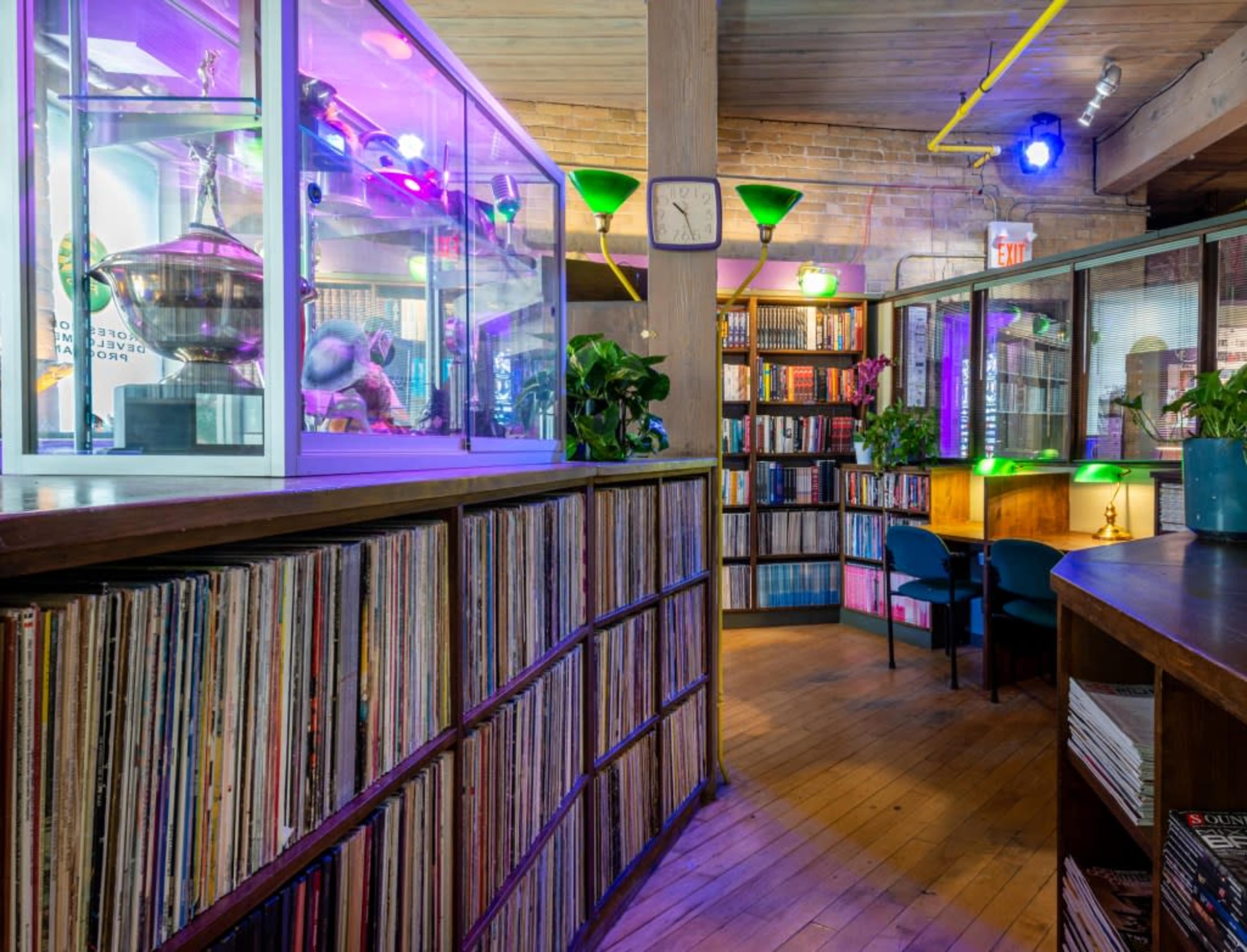 A cozy library space with shelves of books and records, illuminated by colorful lights and featuring a display case.