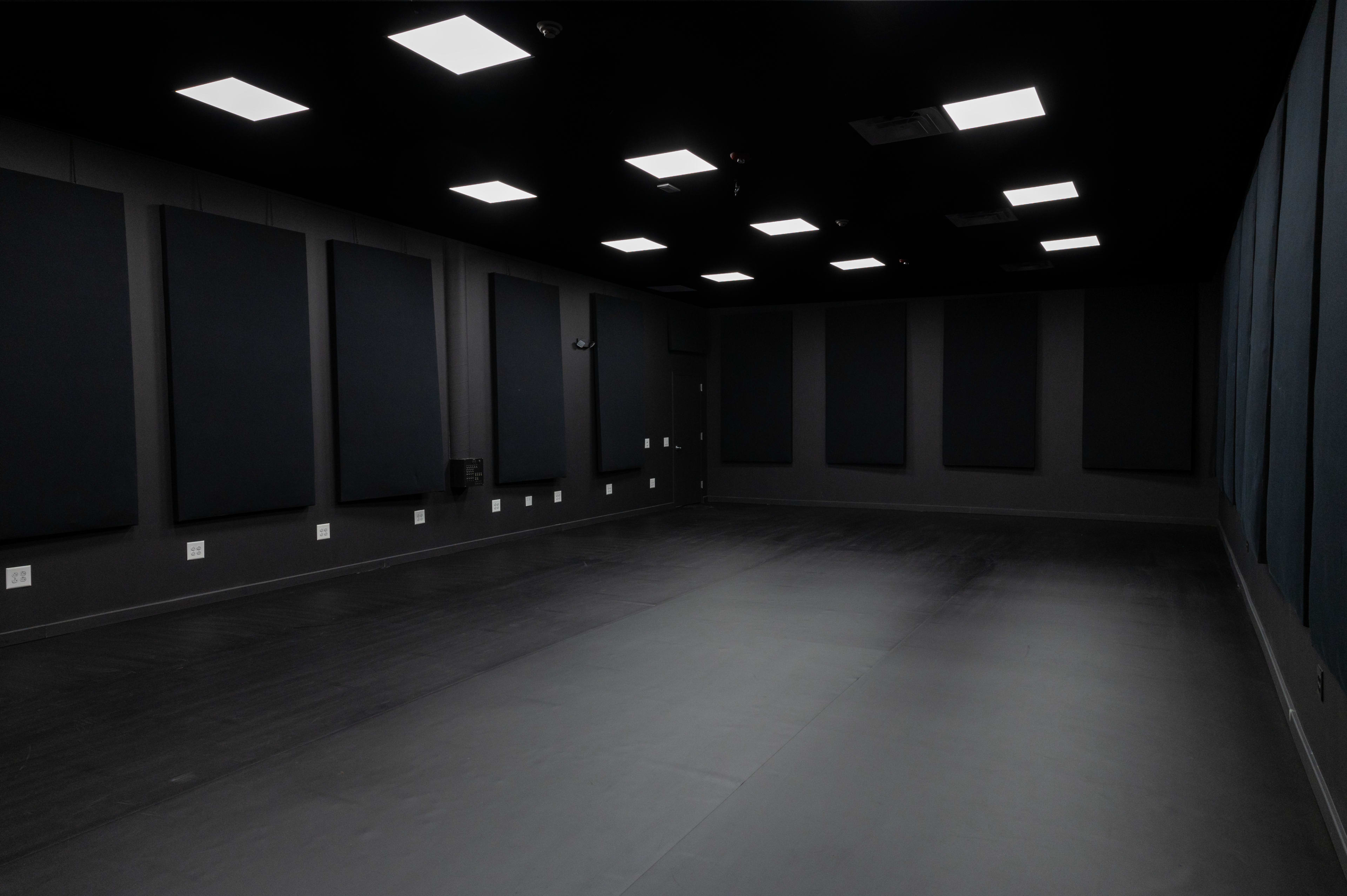 An empty recording studio with soundproofing panels on the walls and a dark, minimalist design.