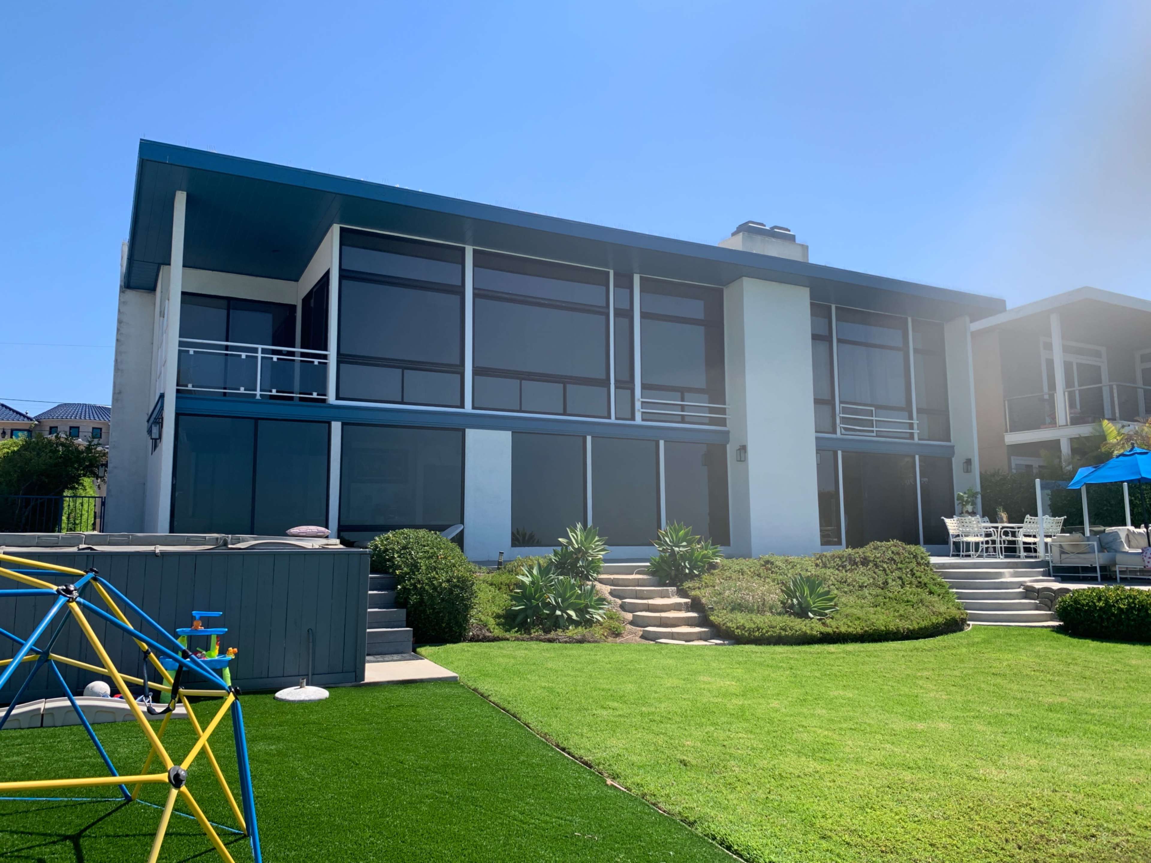 A modern two-story house with large windows and a landscaped lawn features a play structure in the foreground.