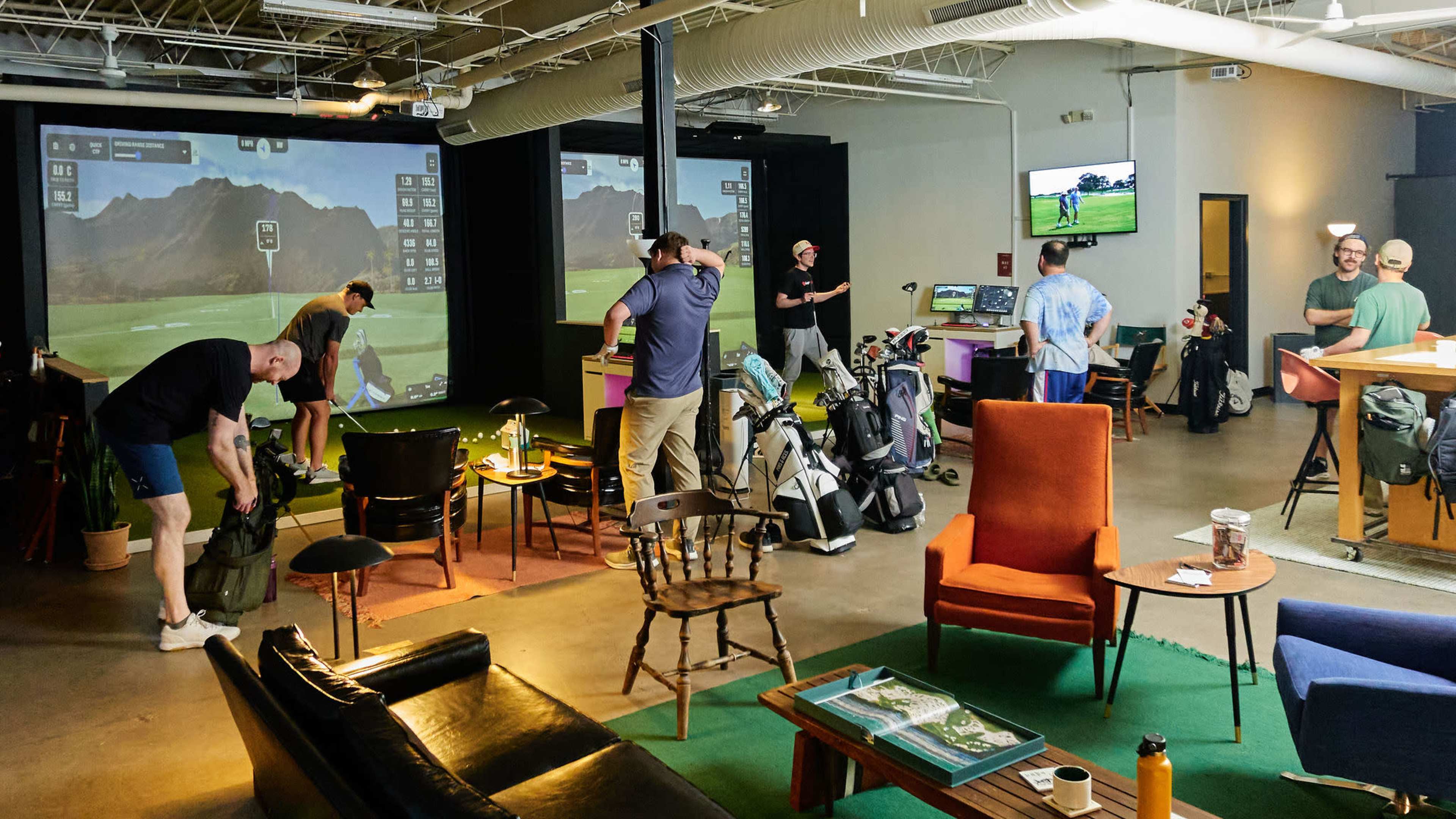 A group of people is engaging in indoor golf practice in a spacious facility that features multiple simulators and comfortable seating areas.