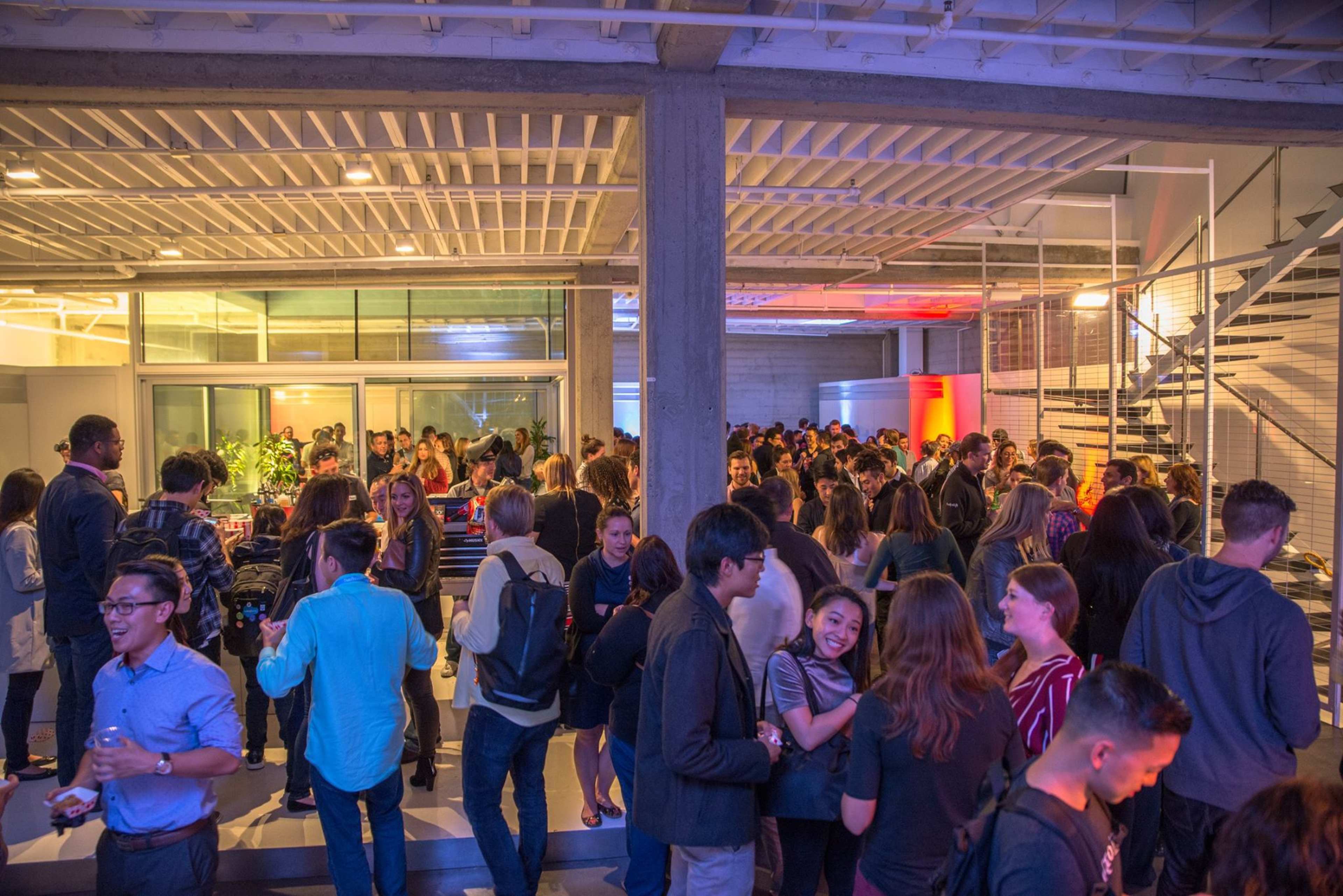 A large group of people socializes at an indoor event featuring modern architecture and bright lighting.