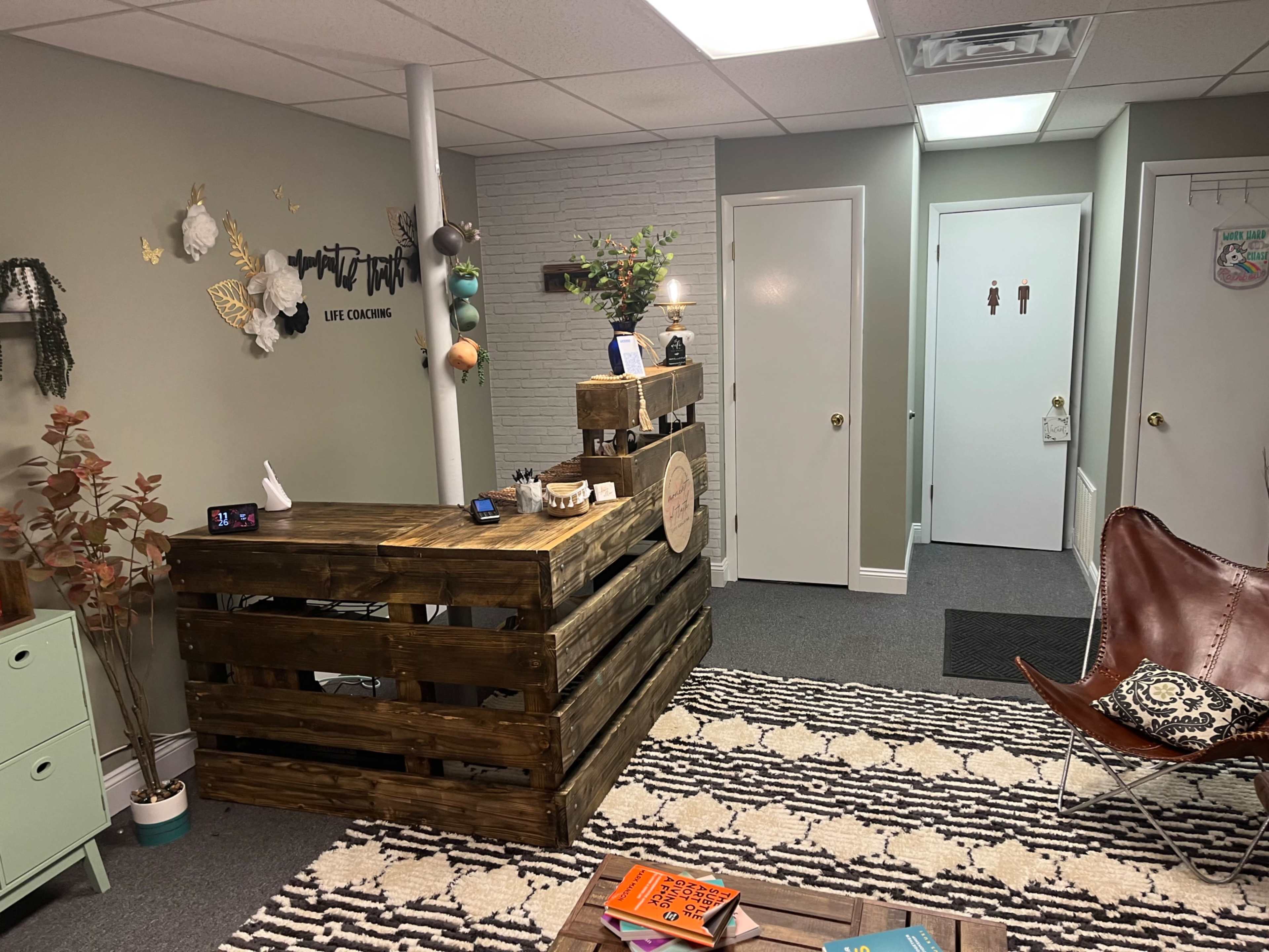 The image shows a modern office reception area featuring a wooden reception desk, a patterned rug, and two doors leading to other rooms.