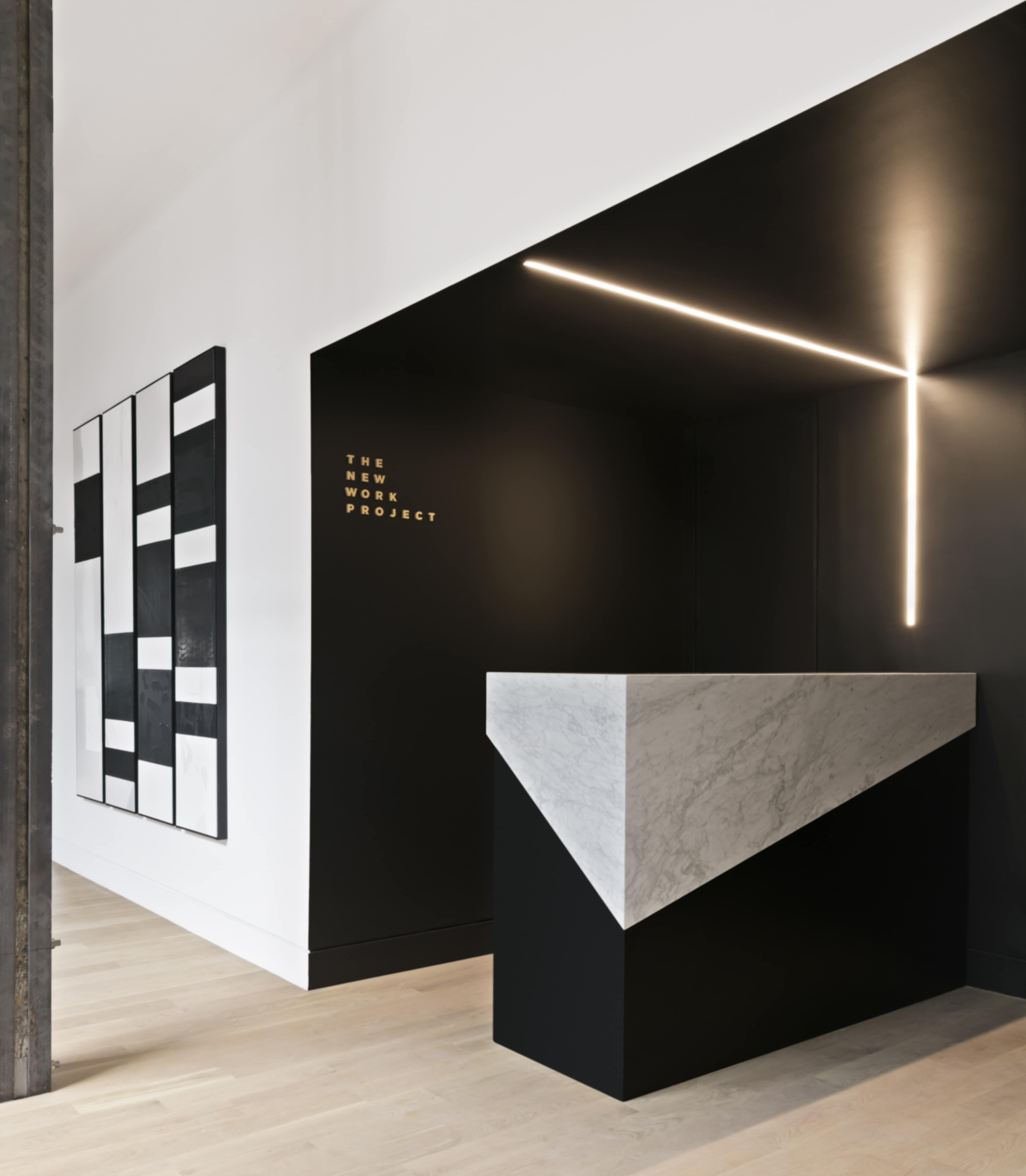 A modern reception area featuring a geometric marble and black counter, against a backdrop of a monochrome artwork on the wall.