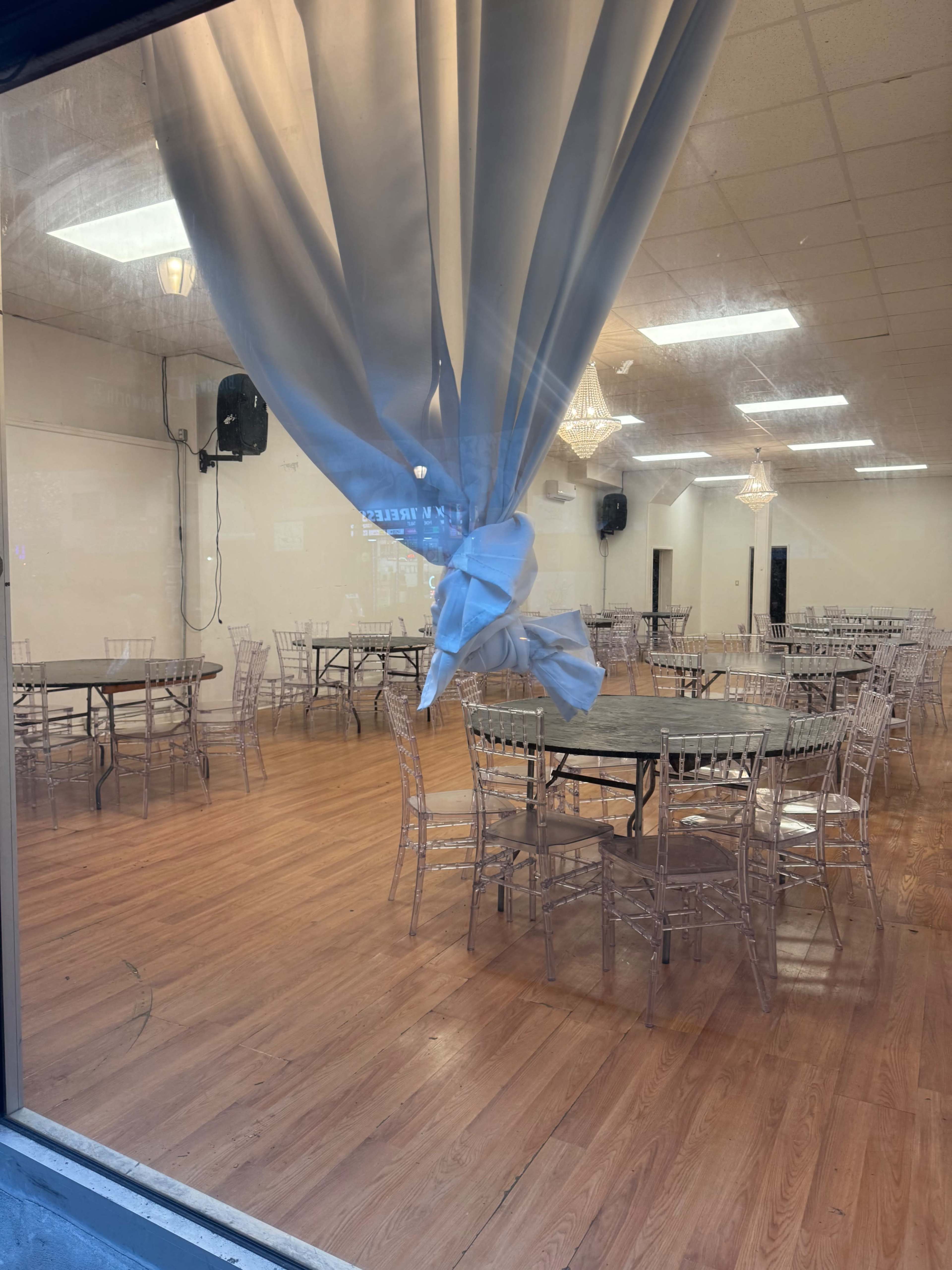 The image shows a spacious indoor venue with round tables set up and a curtain partially drawn, allowing a view of the room.
