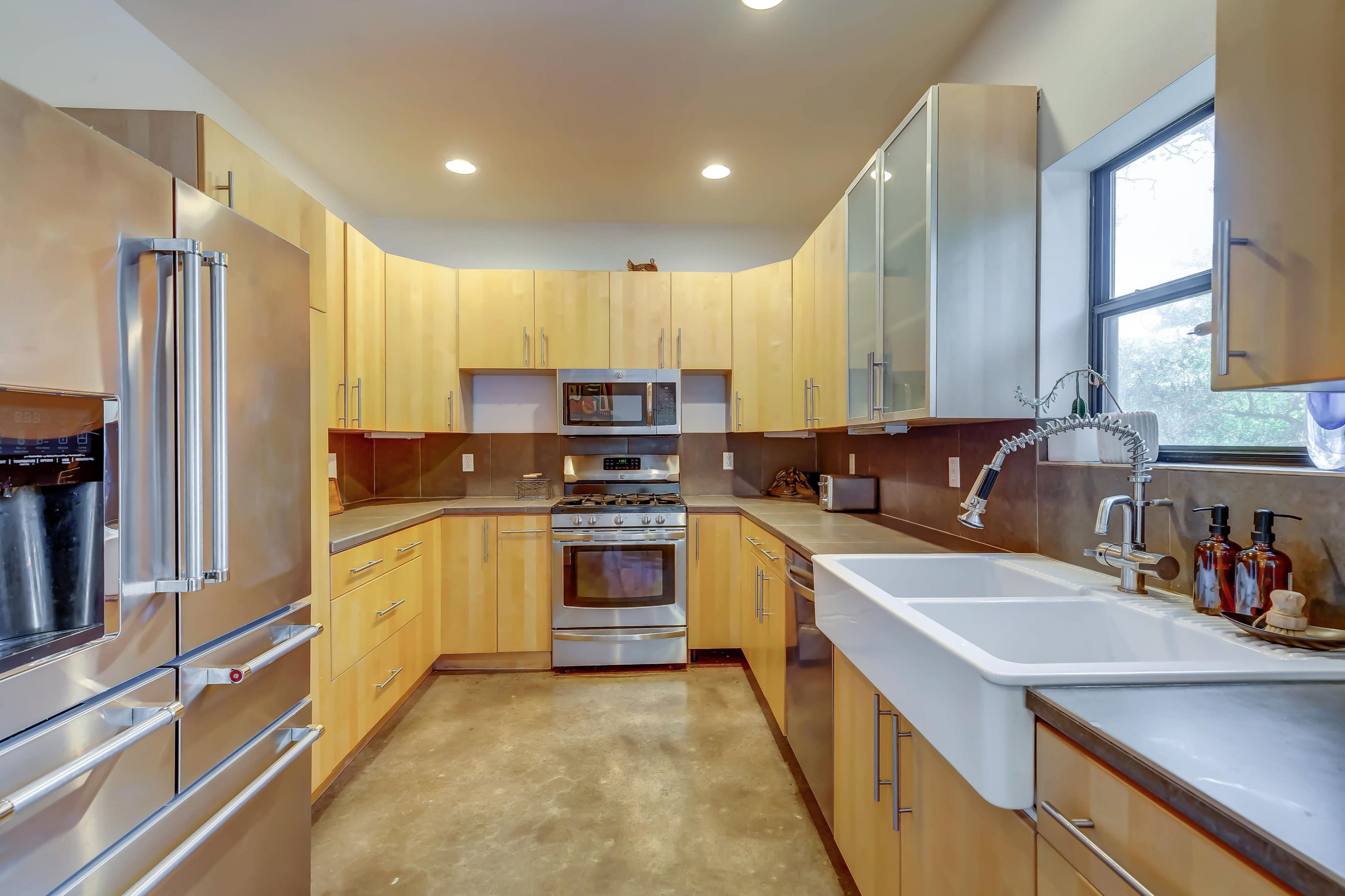 The image shows a modern kitchen with wooden cabinets, stainless steel appliances, and a large farmhouse sink.