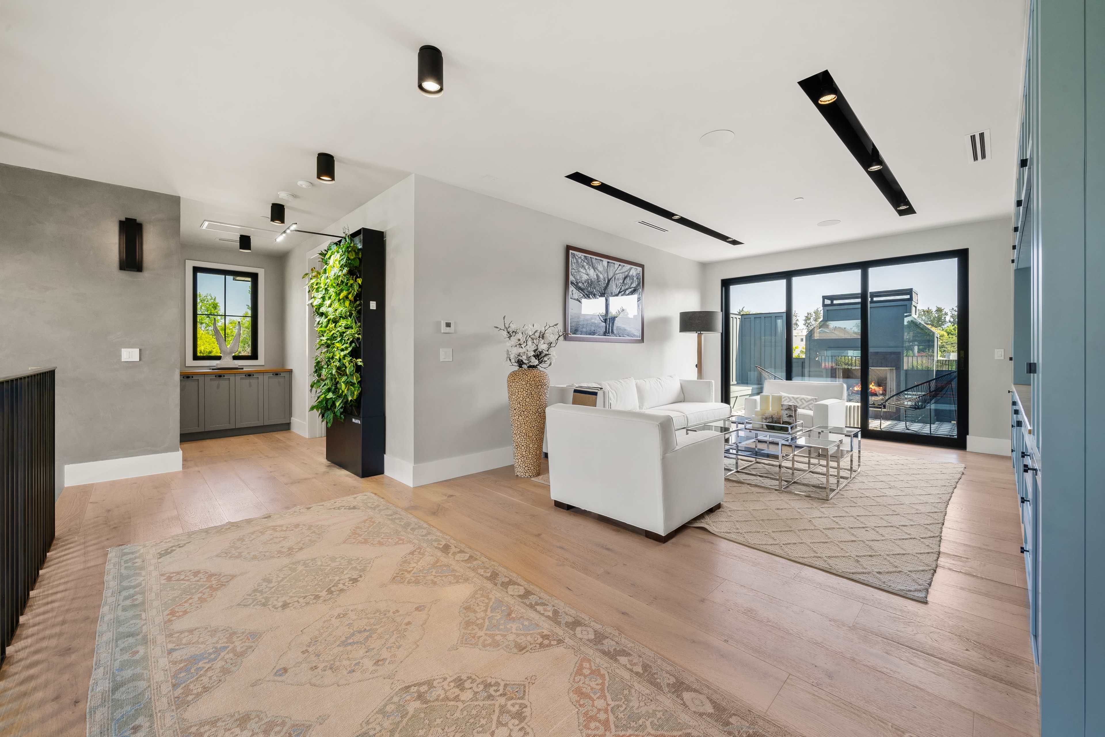 The image shows a modern living space featuring a white sofa, a glass coffee table, and large windows that allow natural light to fill the room.