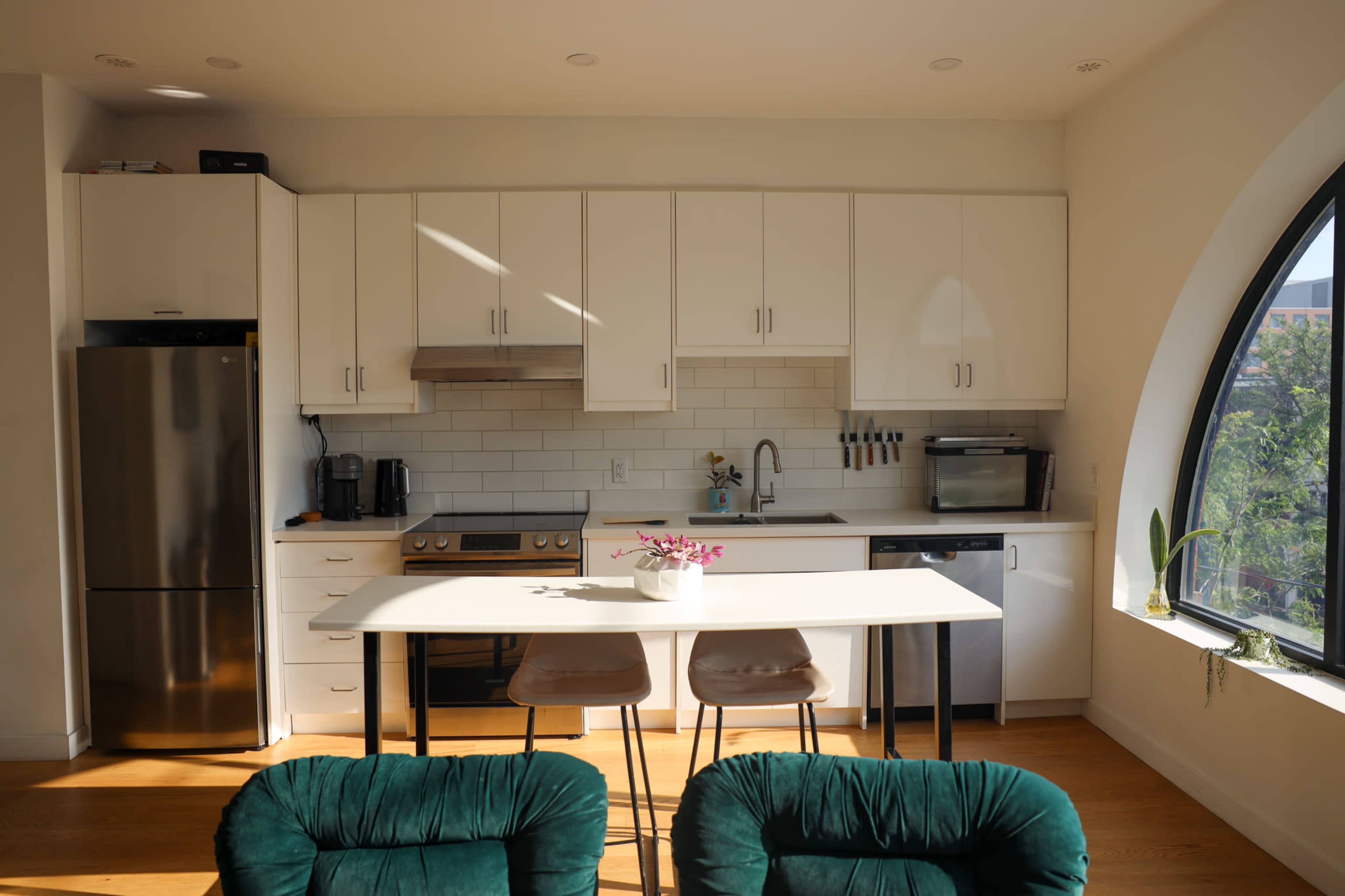 The image shows a modern kitchen with white cabinets, a stainless steel fridge, a stove, and a table with two brown chairs.
