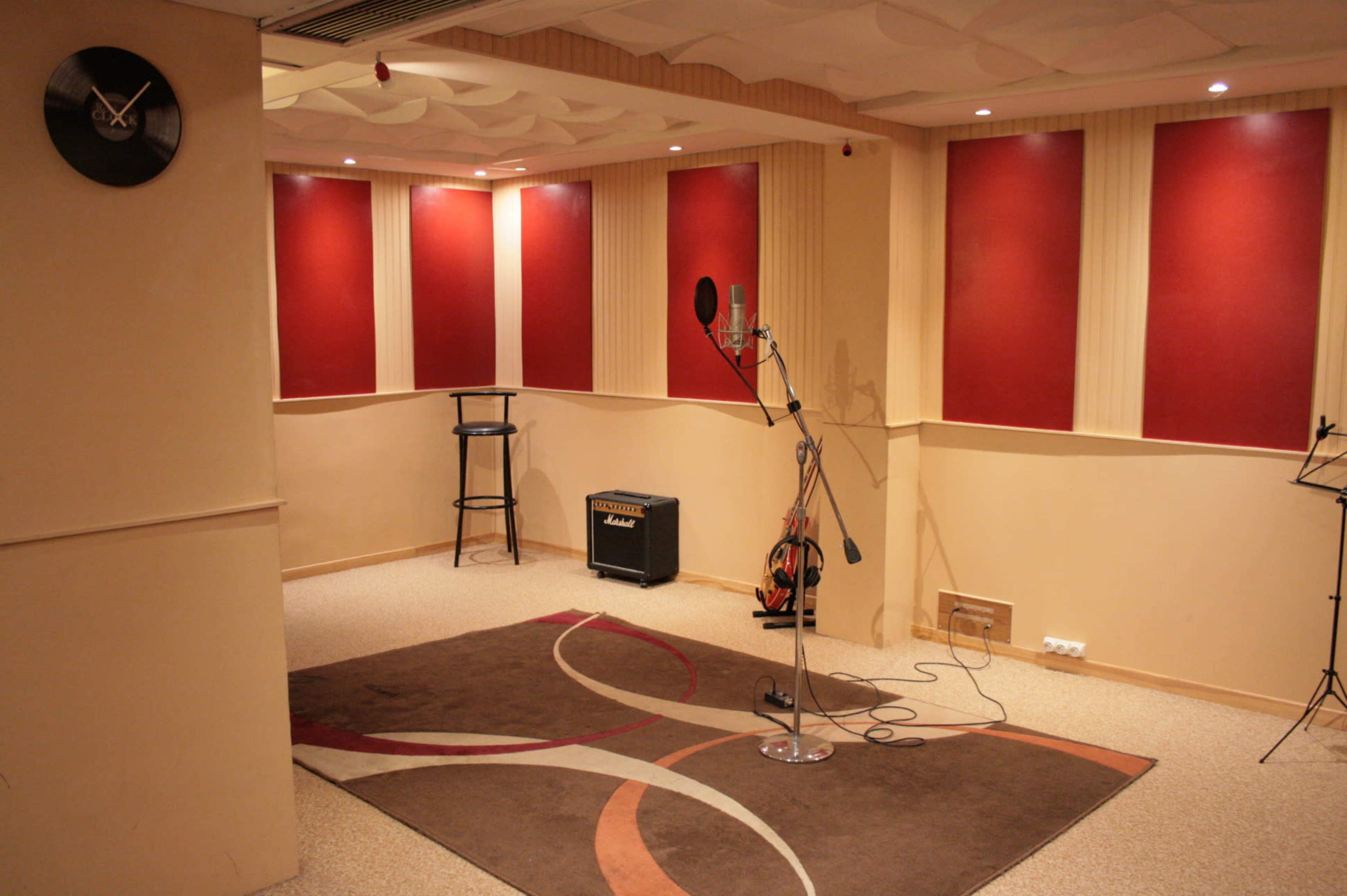 A sound studio with red-accented walls, a microphone on a stand, an amplifier, and a carpeted area.