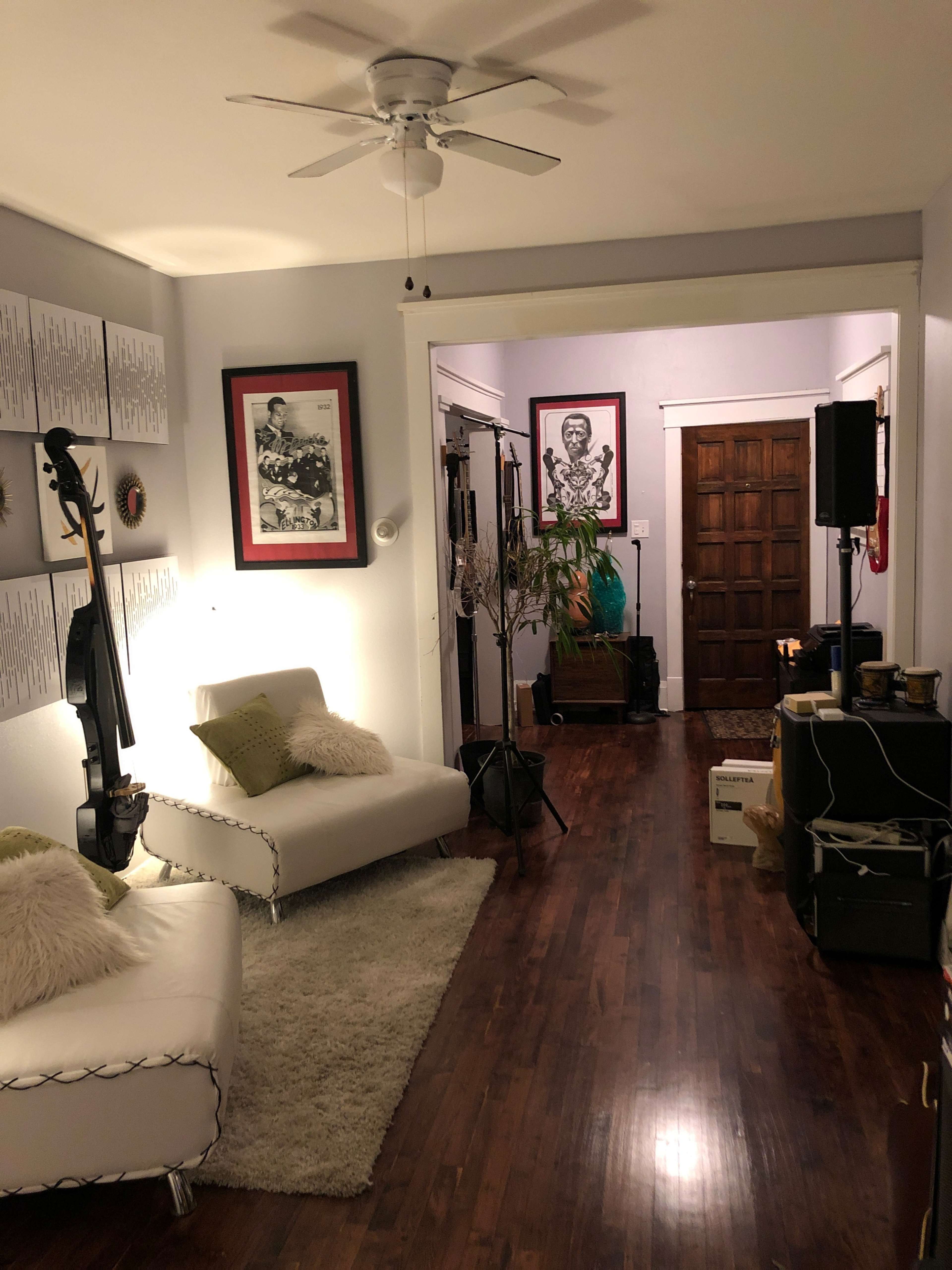 A living room with a white sofa, a ceiling fan, and a hallway leading to another room with wooden doors and framed art on the walls.