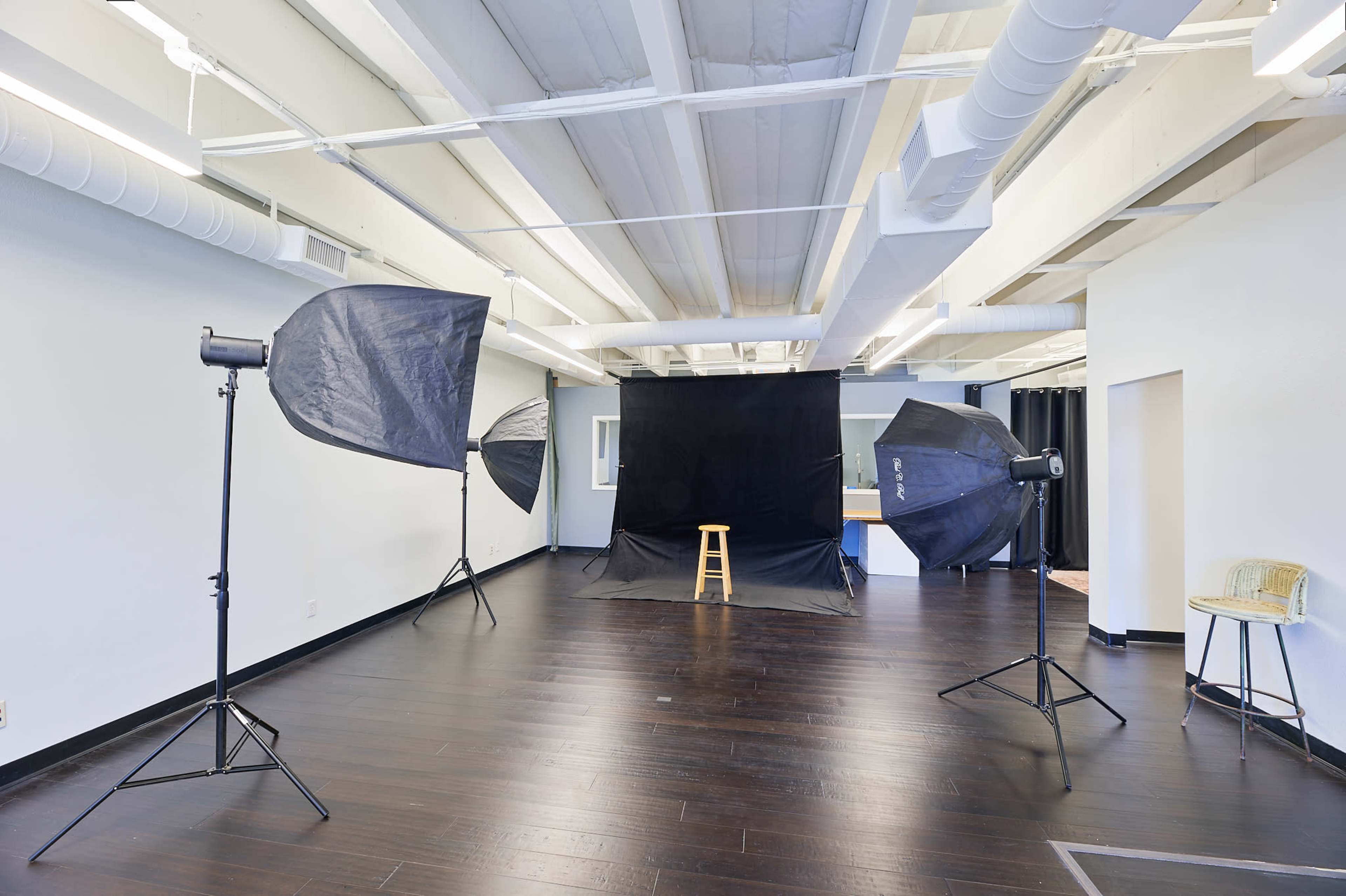 A photography studio with a black backdrop, a wooden stool, and two large softboxes positioned on either side.