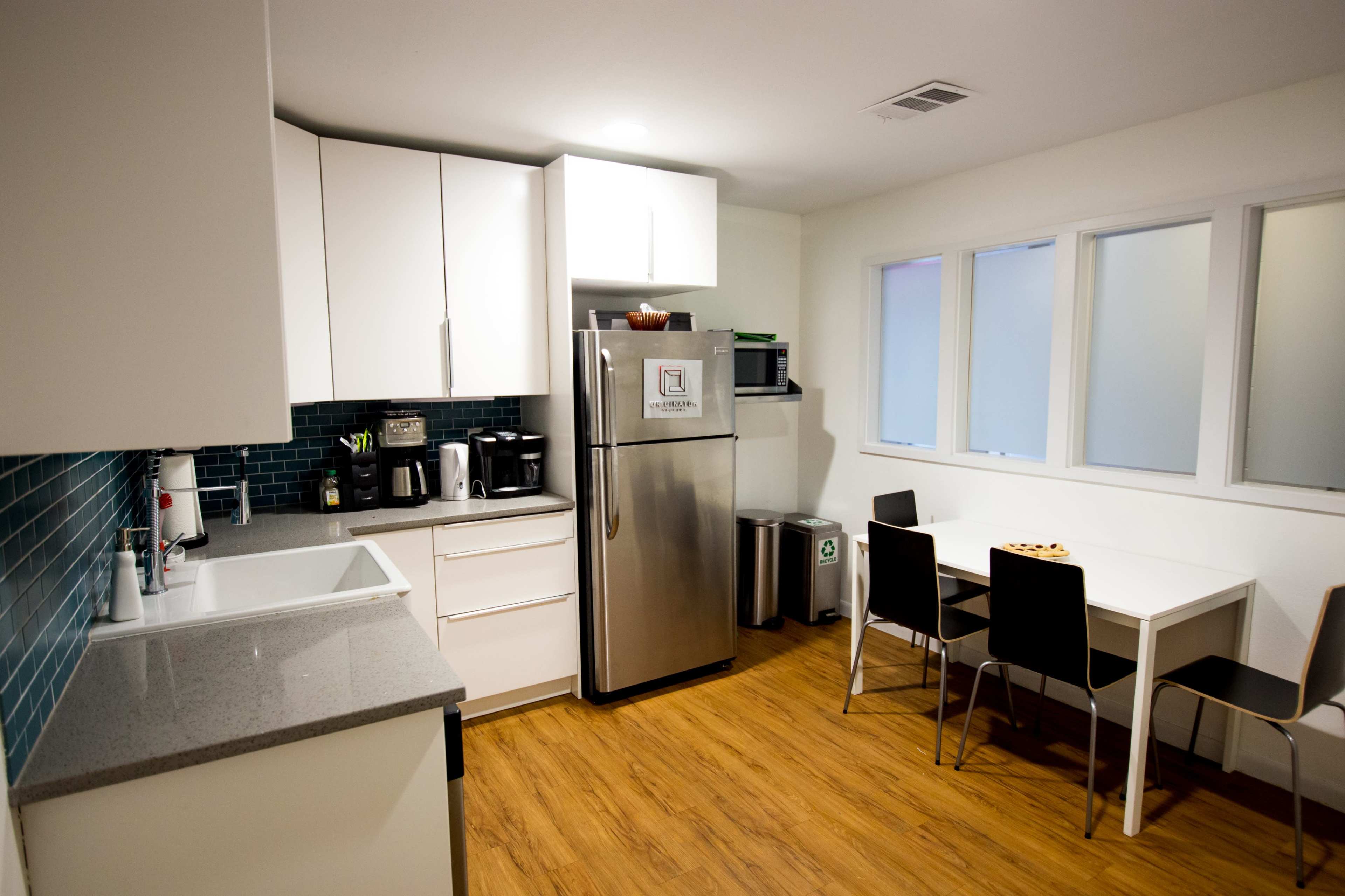 A modern kitchen features white cabinets, a stainless steel refrigerator, a sink, and a small dining table with chairs.
