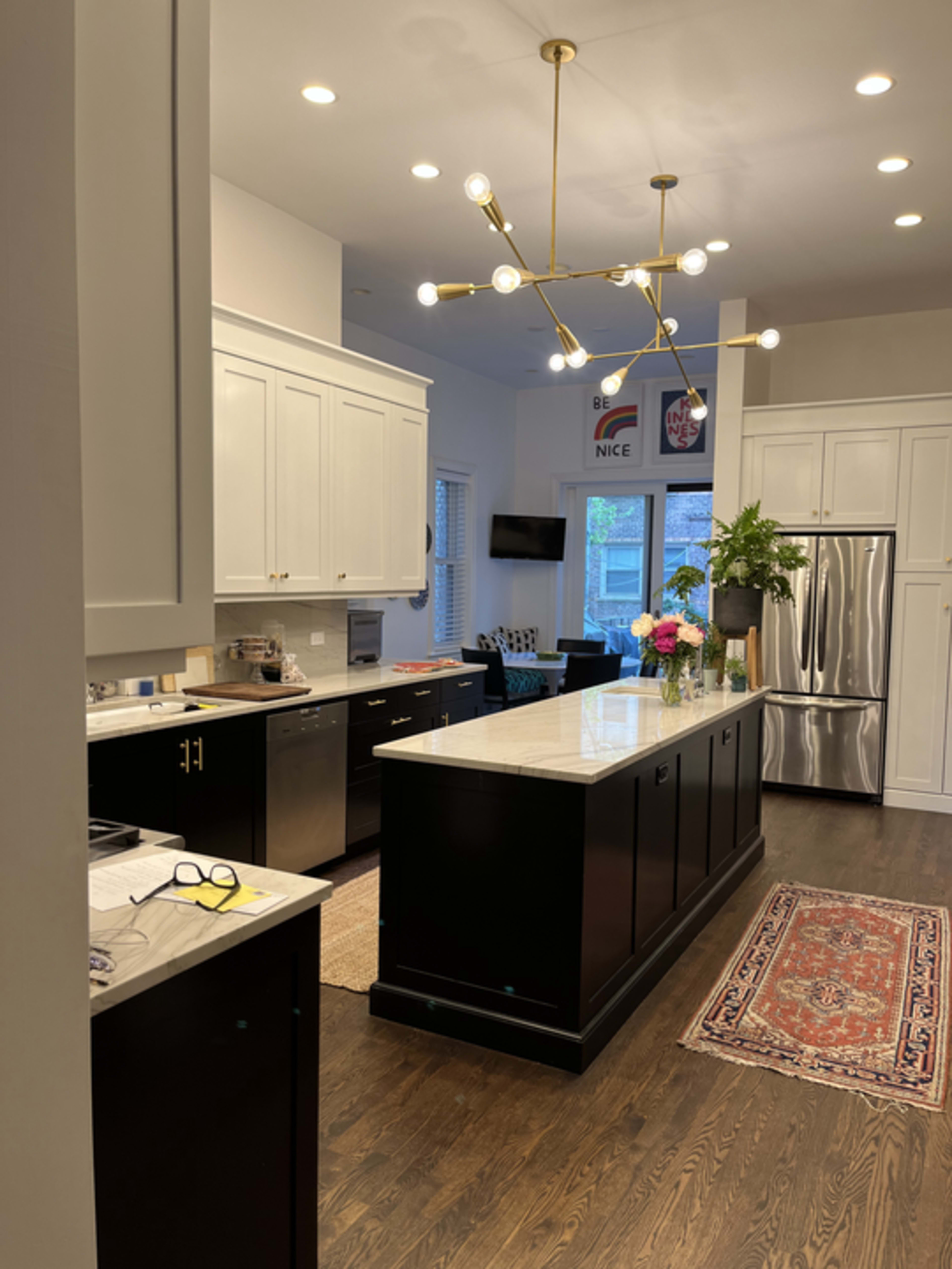 A modern kitchen features a central island with a marble countertop, black cabinetry, stainless steel appliances, and a pendant light fixture.