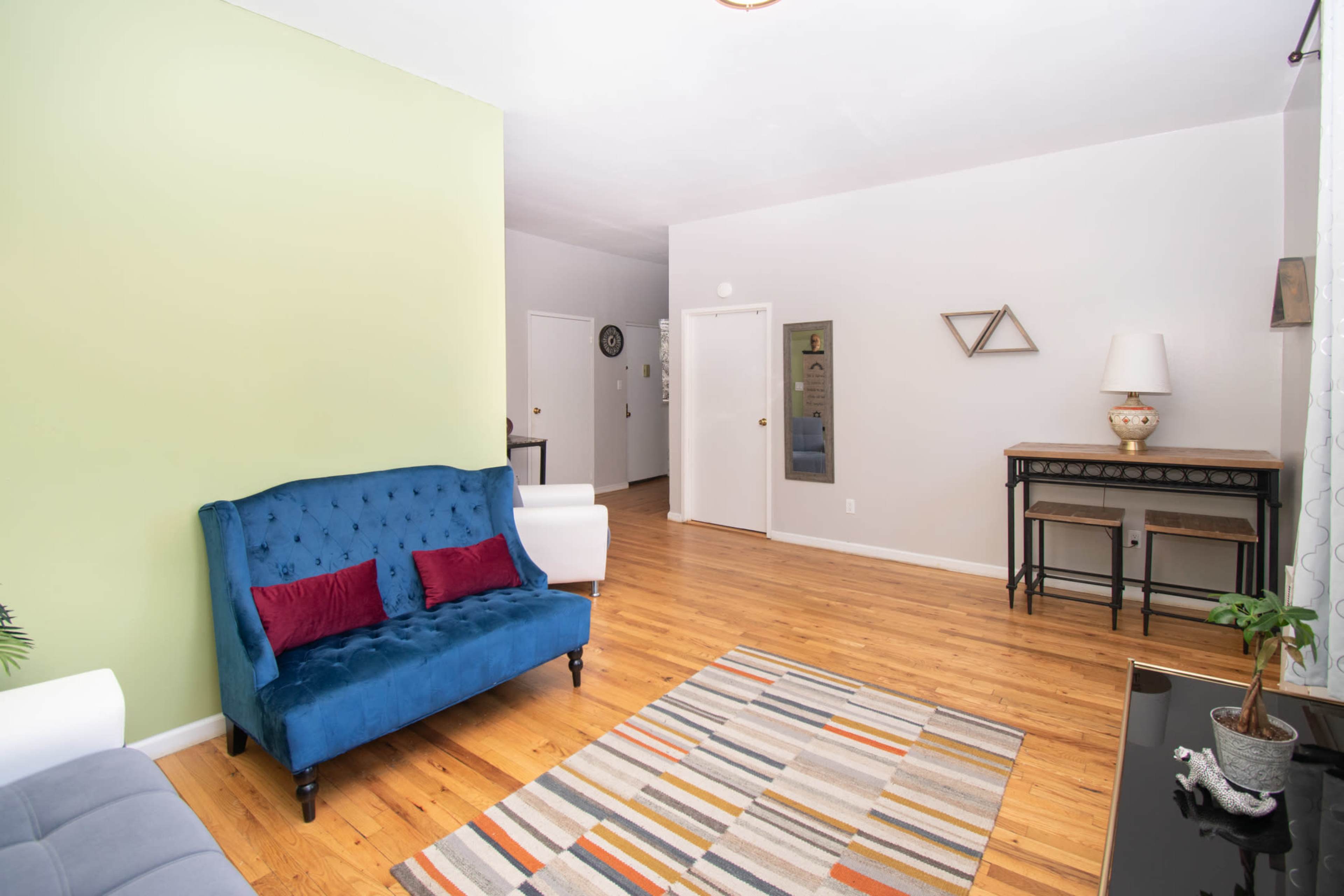 A living room featuring a blue tufted sofa, a striped rug, a wooden table, and a green accent wall.