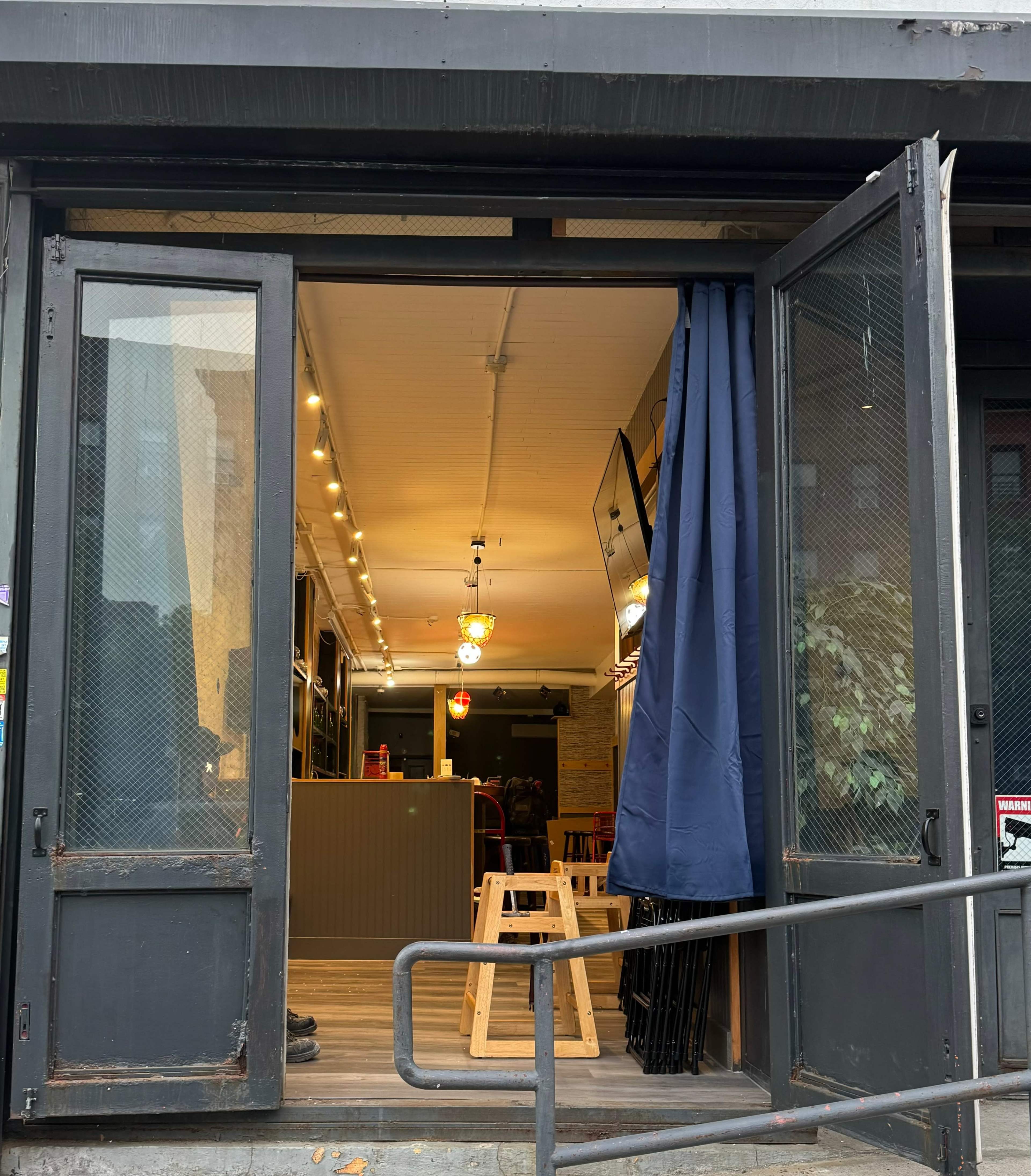 The entrance of a café features open doors with a curtain, revealing an interior with soft lighting and a wooden floor.
