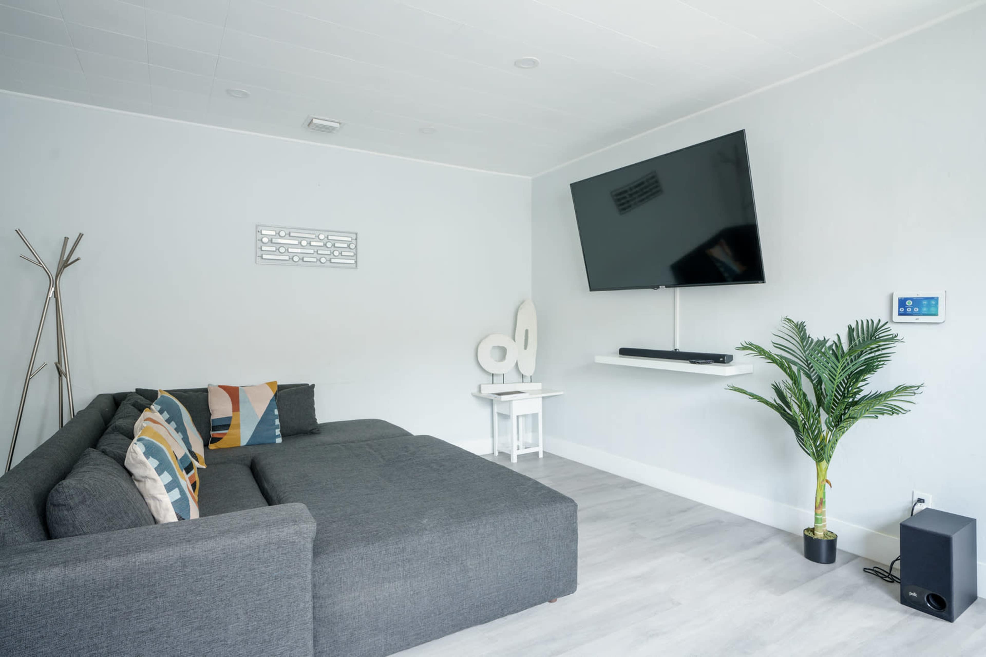 A modern living room features a gray sectional sofa, a mounted flat-screen TV, and a small indoor plant beside a white side table.