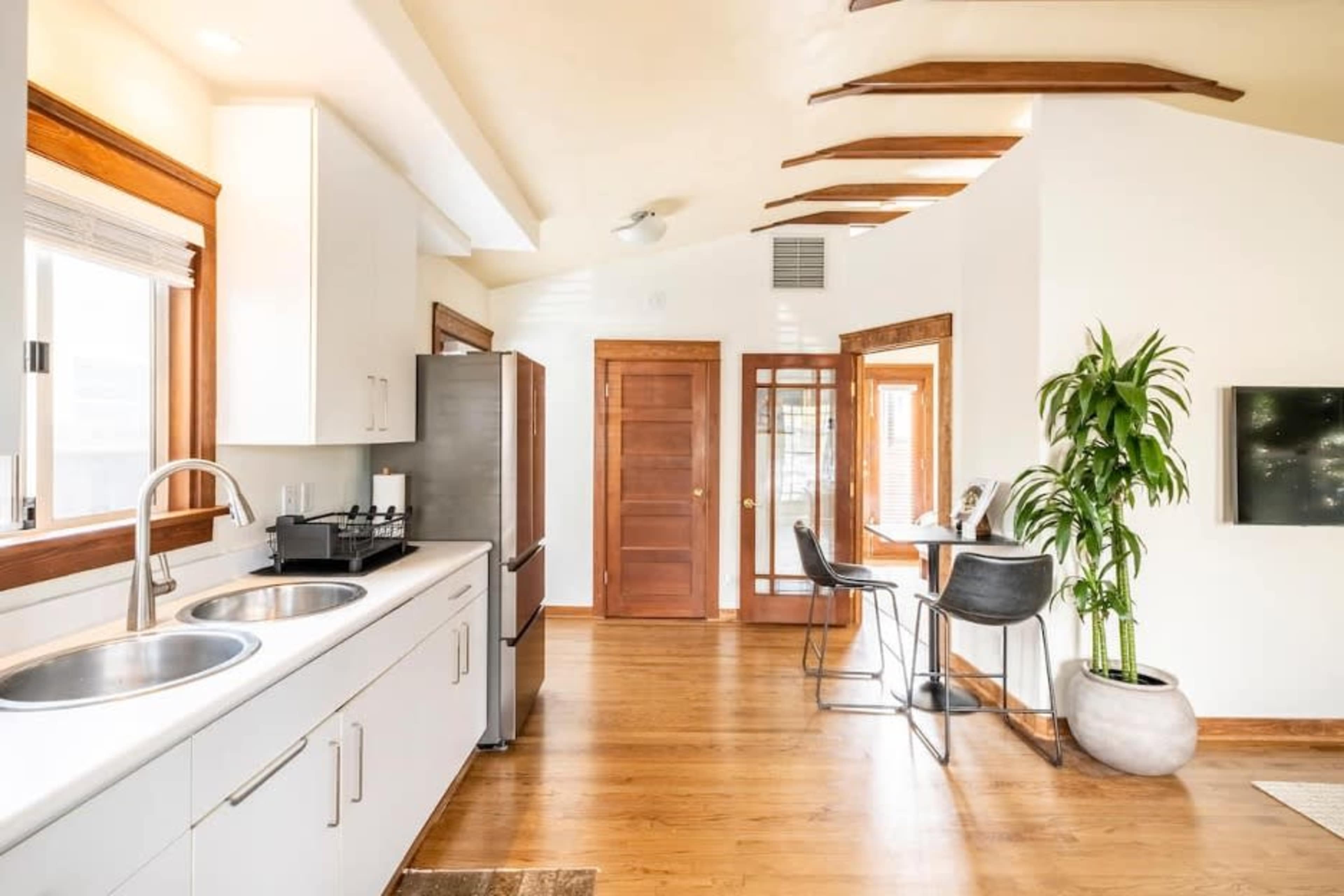 A modern kitchen and dining area with a double sink, stainless steel appliances, and a small table with chairs beside a large window.